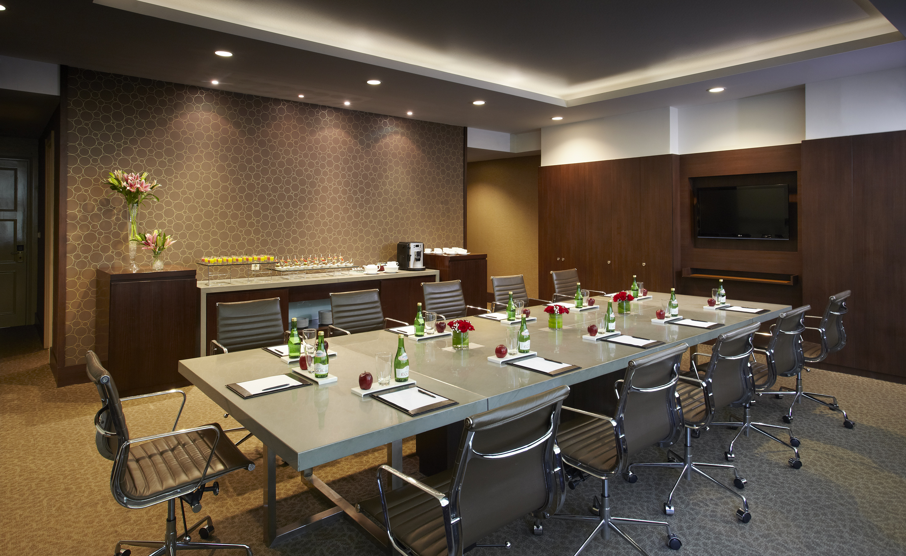Modern conference room with long table, leather chairs, TV, and snacks.