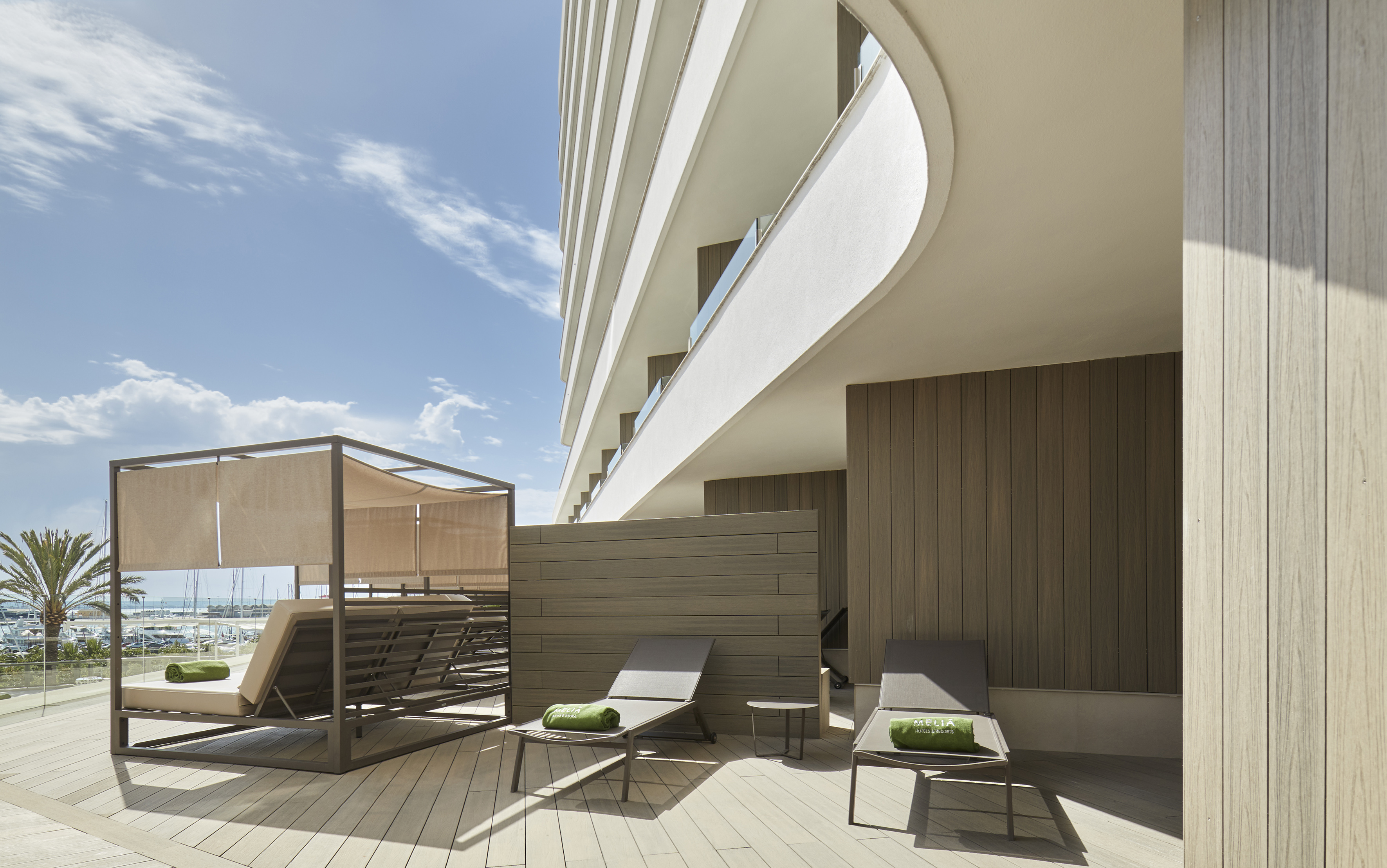 Melia hotel terrace with modern daybed, lounge chairs, and marina views.