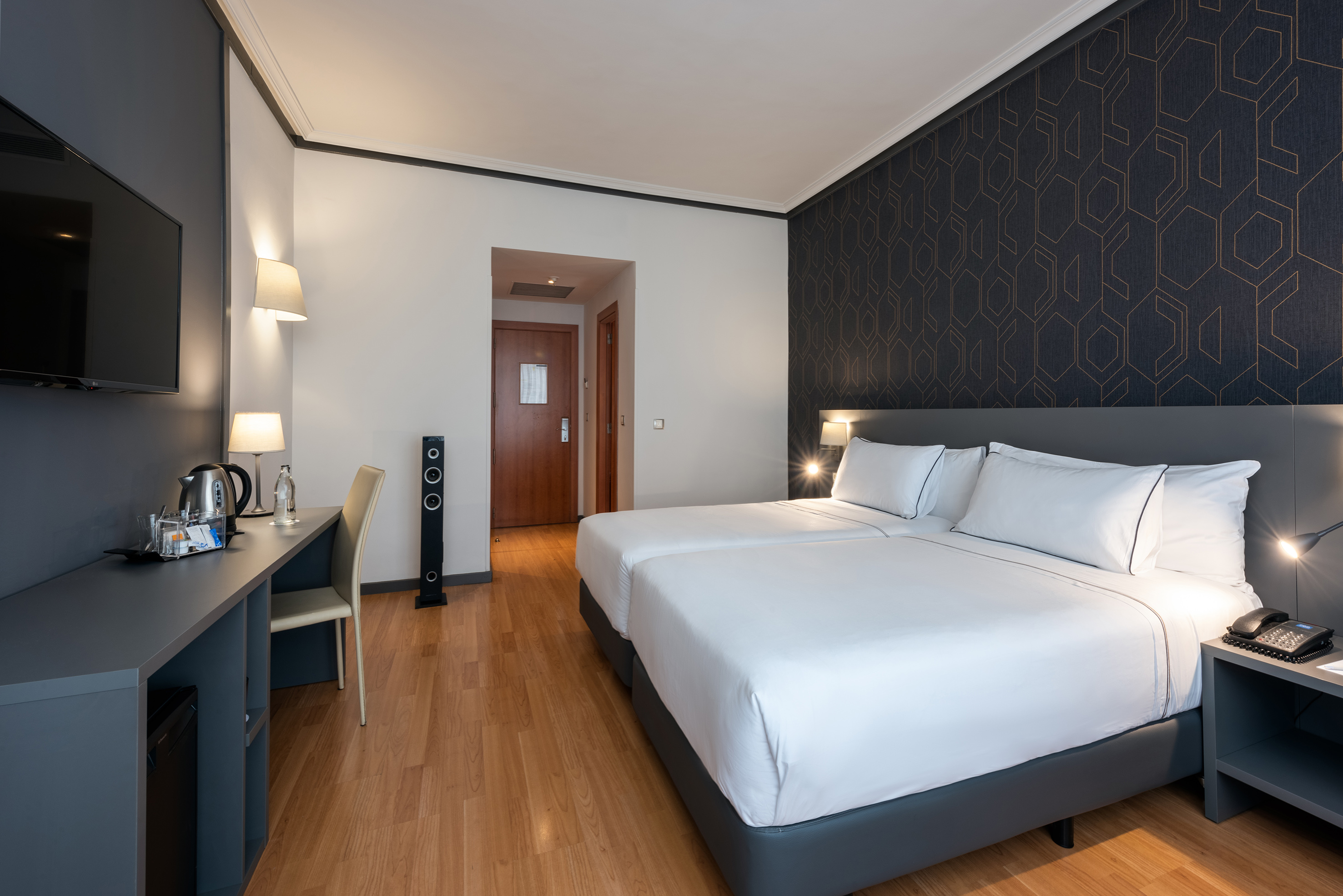 Comfortable hotel room with twin beds, dark decor, desk, and TV.