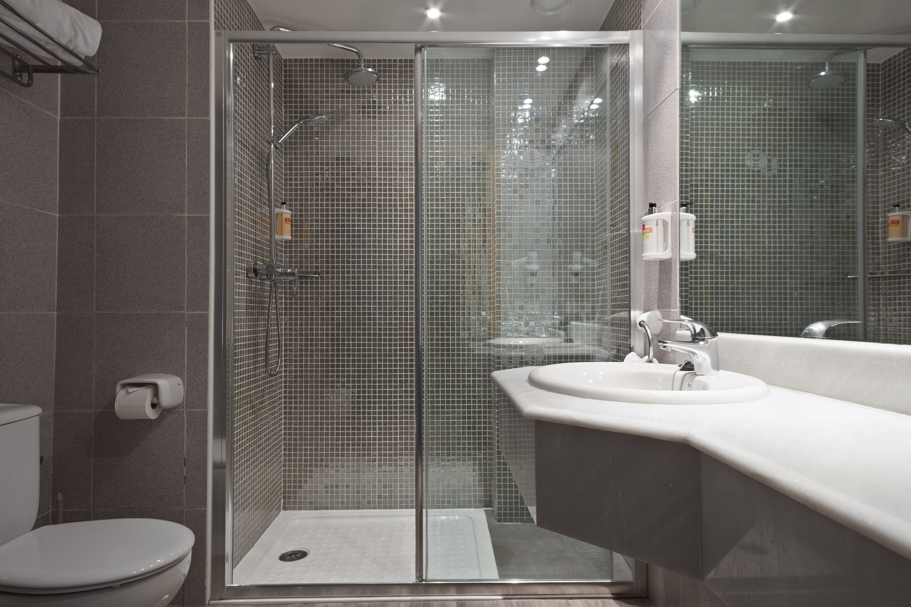 Modern bathroom with walk-in shower, mosaic tiles, white sink, and toilet.