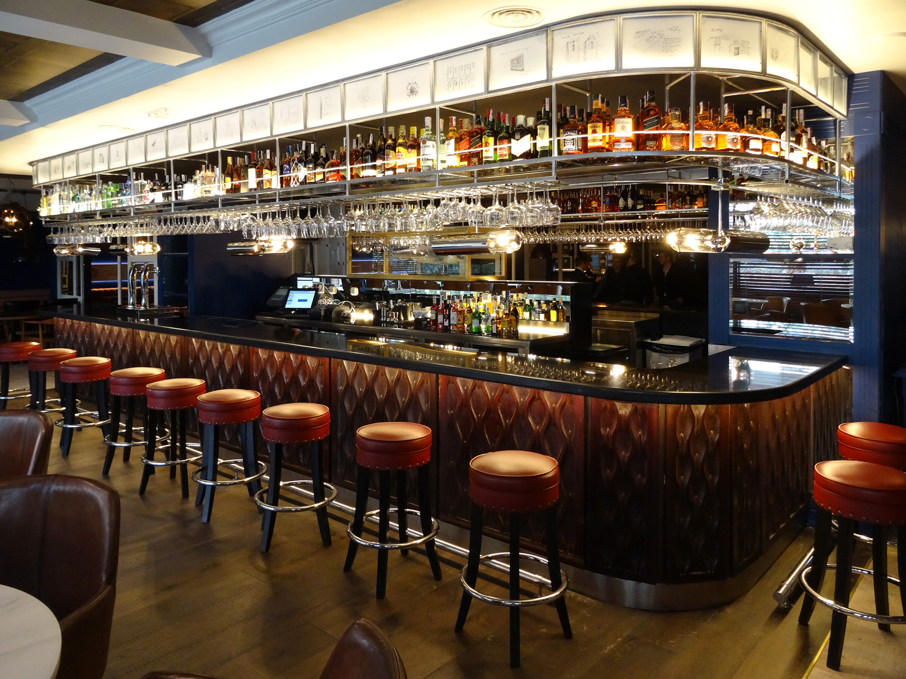 Elegant bar counter with spirits bottles, hanging glasses, and red stools.