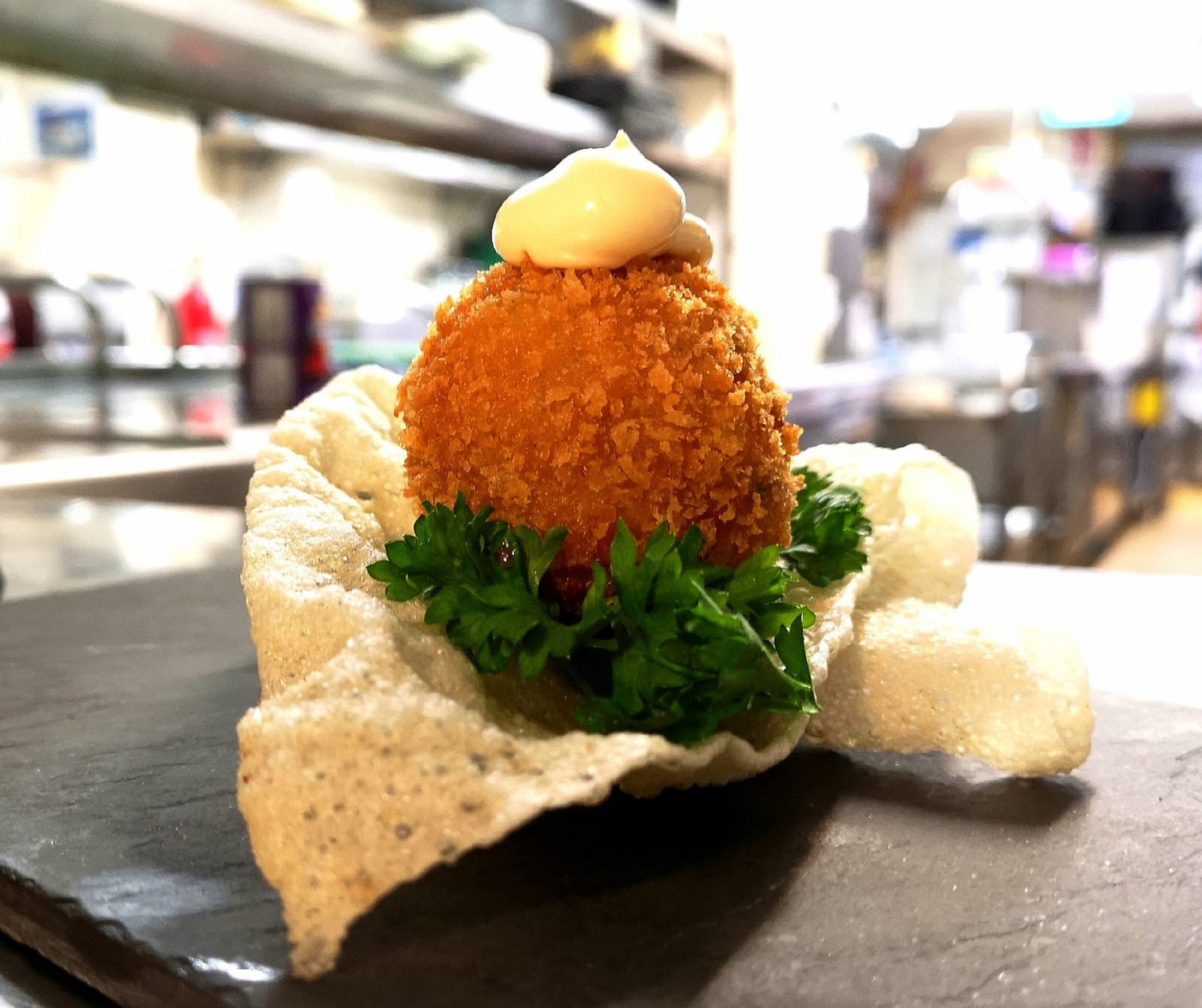 Golden fried croquette appetizer with aioli, parsley, on crisp chip and slate.