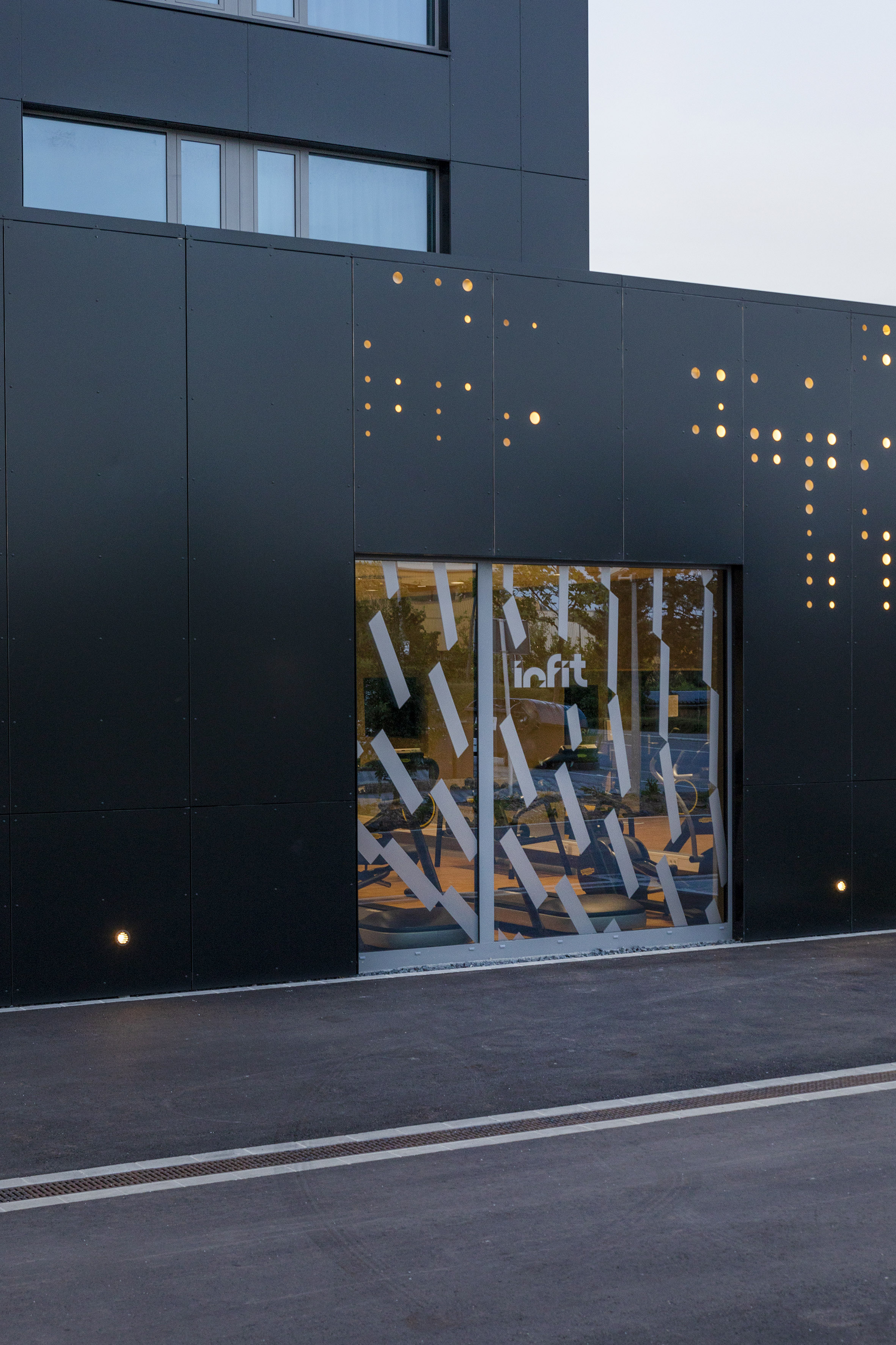 Modern black building facade with glowing dots and "infit" gym window.