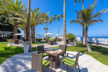 a table and chairs outside with palm trees and a beach in the background