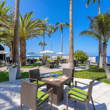 a table and chairs outside with palm trees and a beach in the background