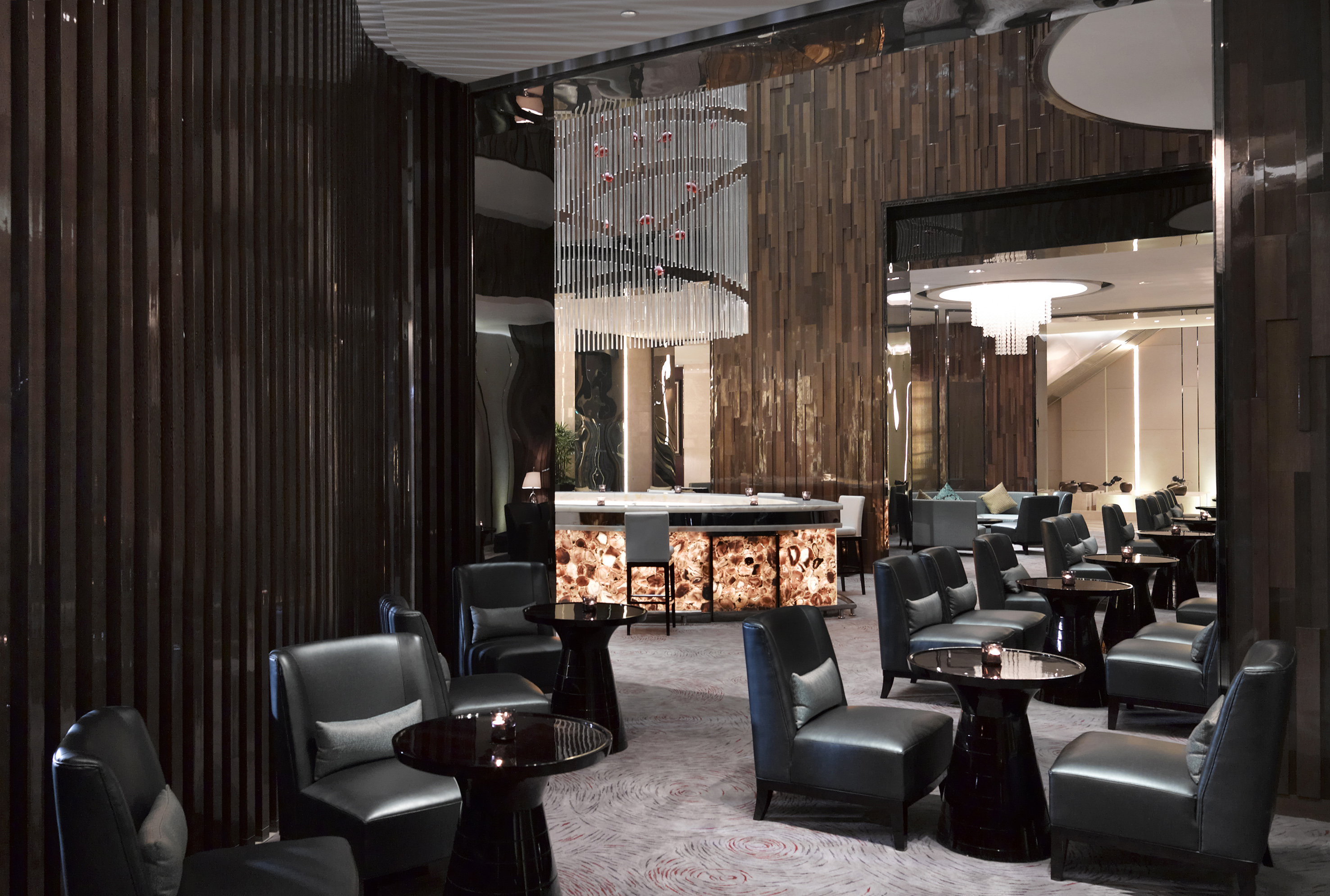 Dark, luxurious hotel bar interior with leather armchairs and backlit stone bar.