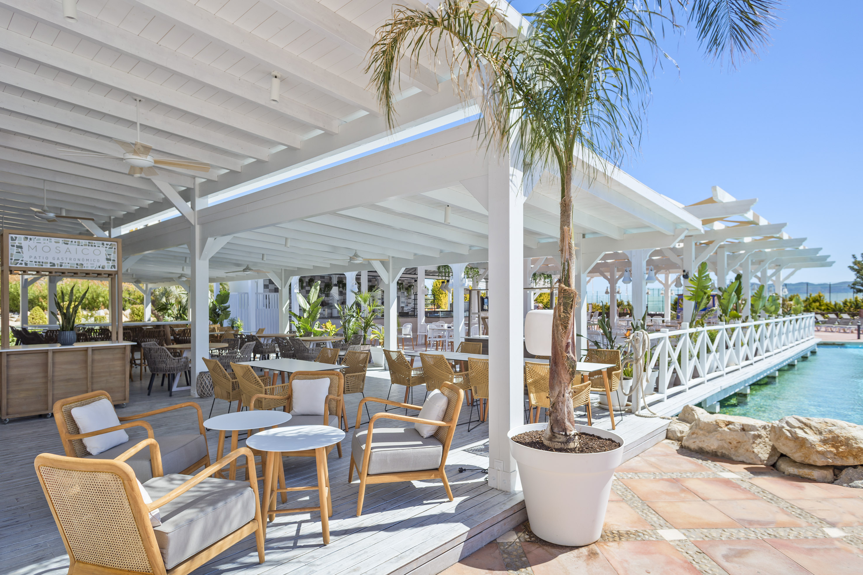 Tropical resort outdoor dining patio with white pergola and pool.