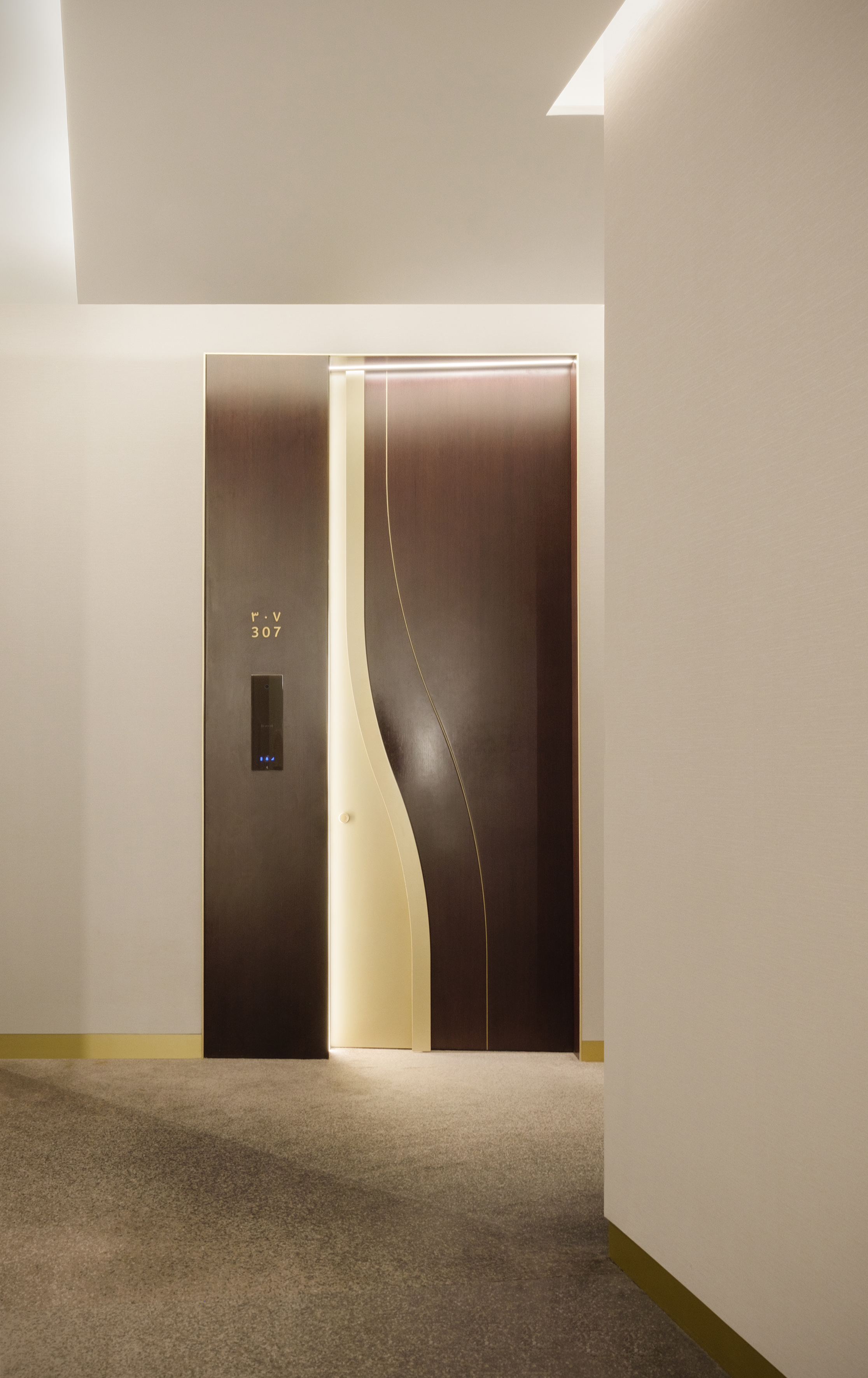Modern dark door 307 with curved illuminated panel in a hotel hallway.