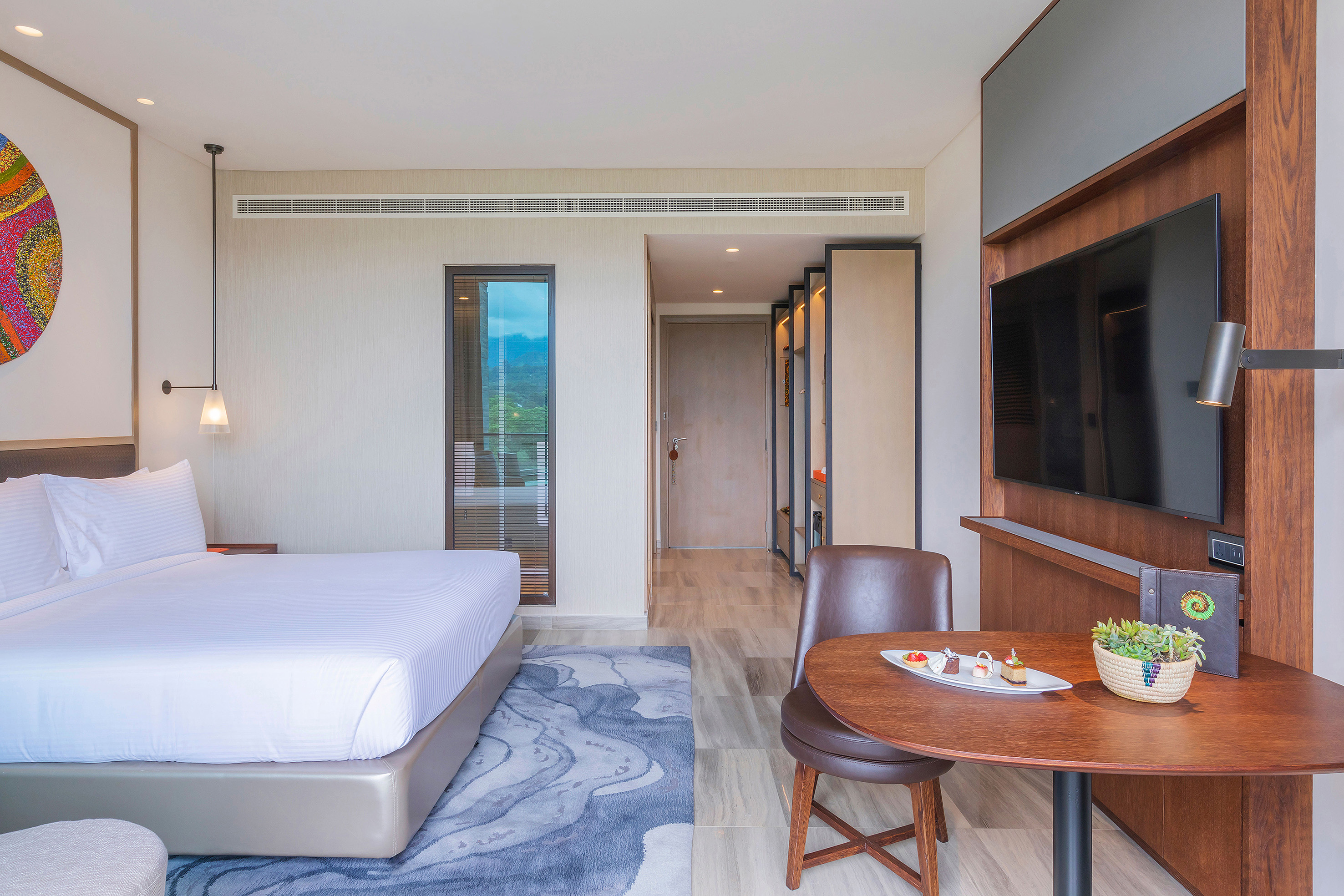 Modern hotel room with large bed, flat-screen TV, and small table with desserts.