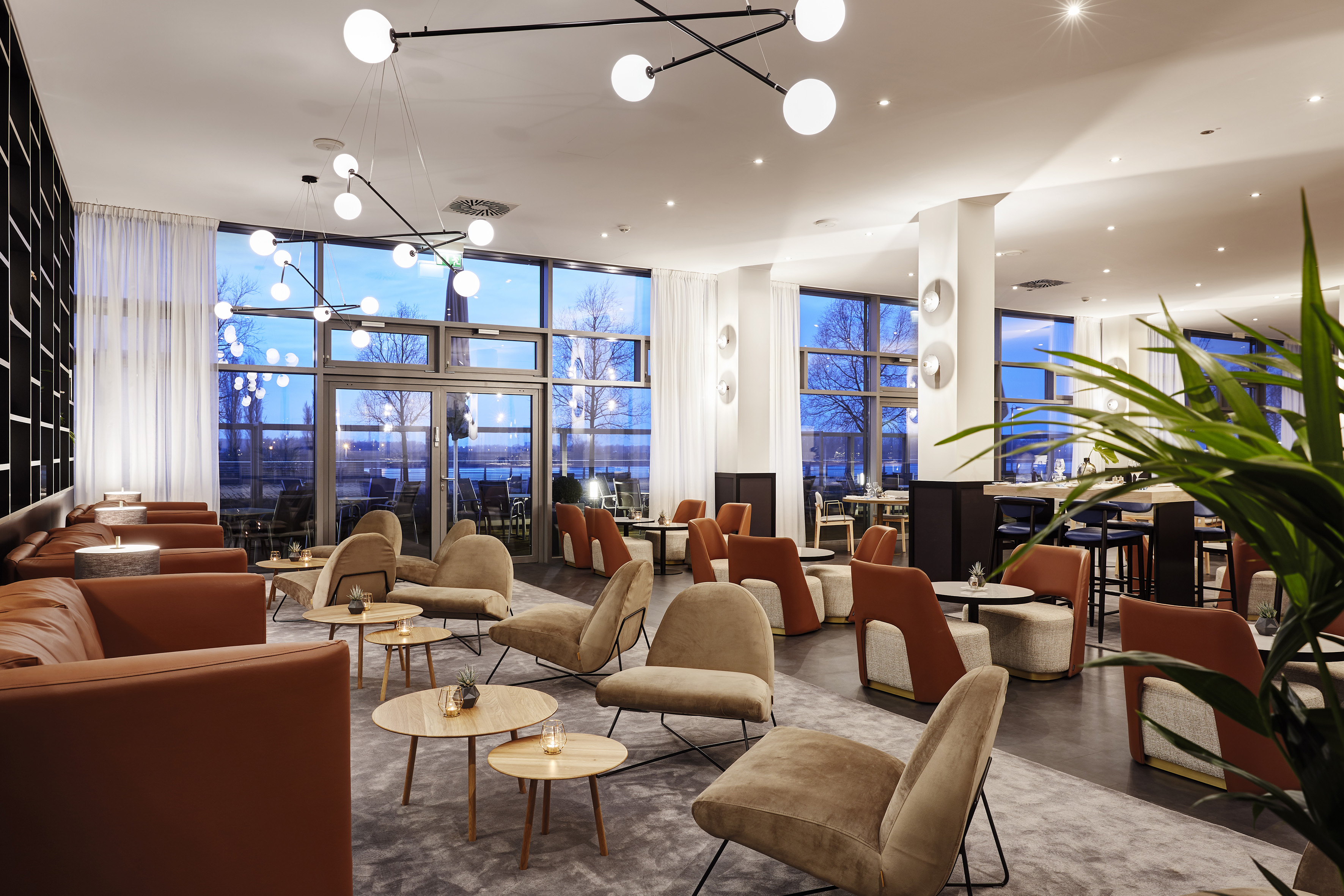 Modern hotel lounge with varied seating, modern lighting, and water view.