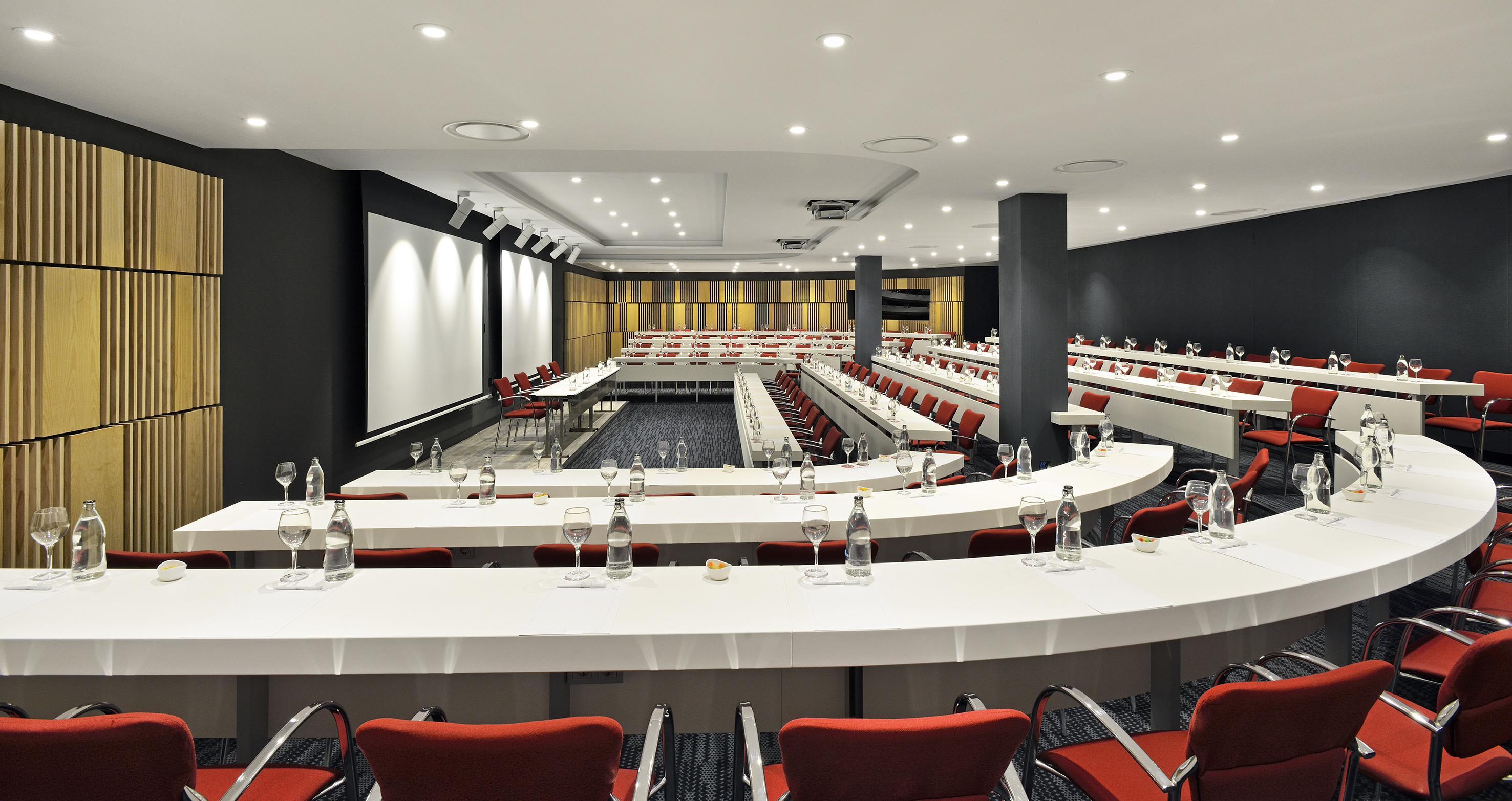 Modern conference room with red chairs, white tables, and projection screen.