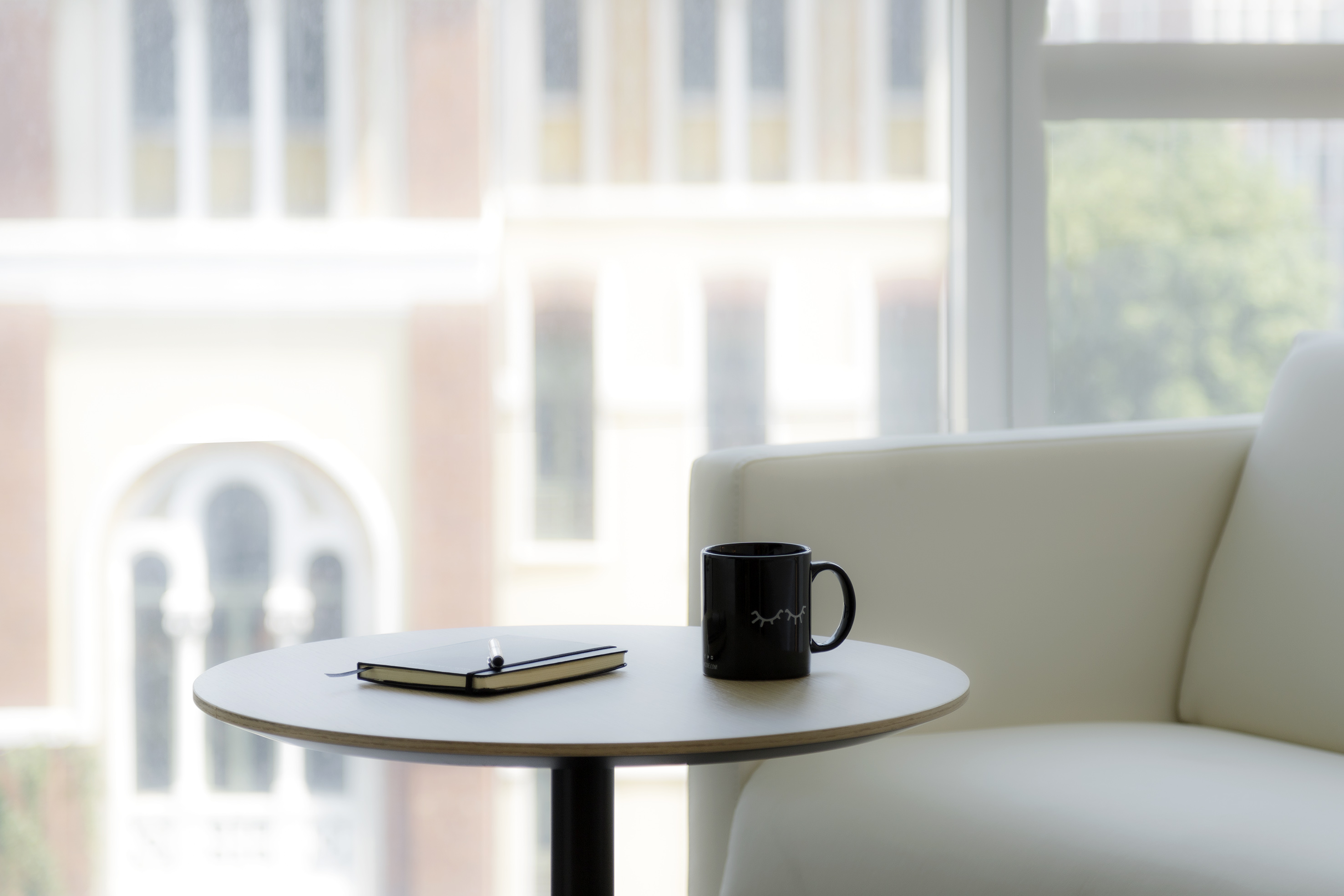 Modern lounge: black mug, notebook on side table, cream armchair by bright window.