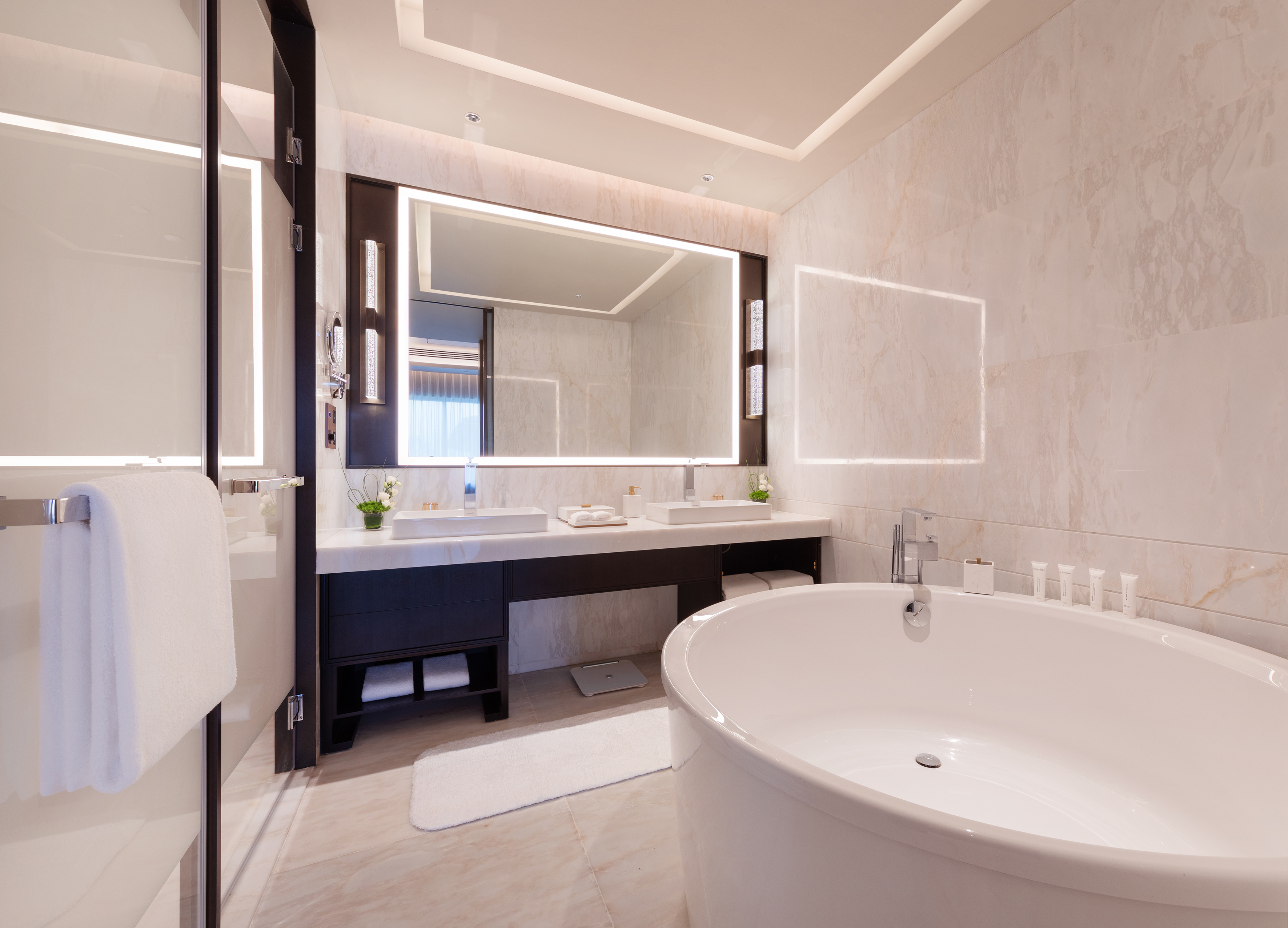 Modern bathroom with freestanding bathtub, double vanity, lighted mirror, and marble.
