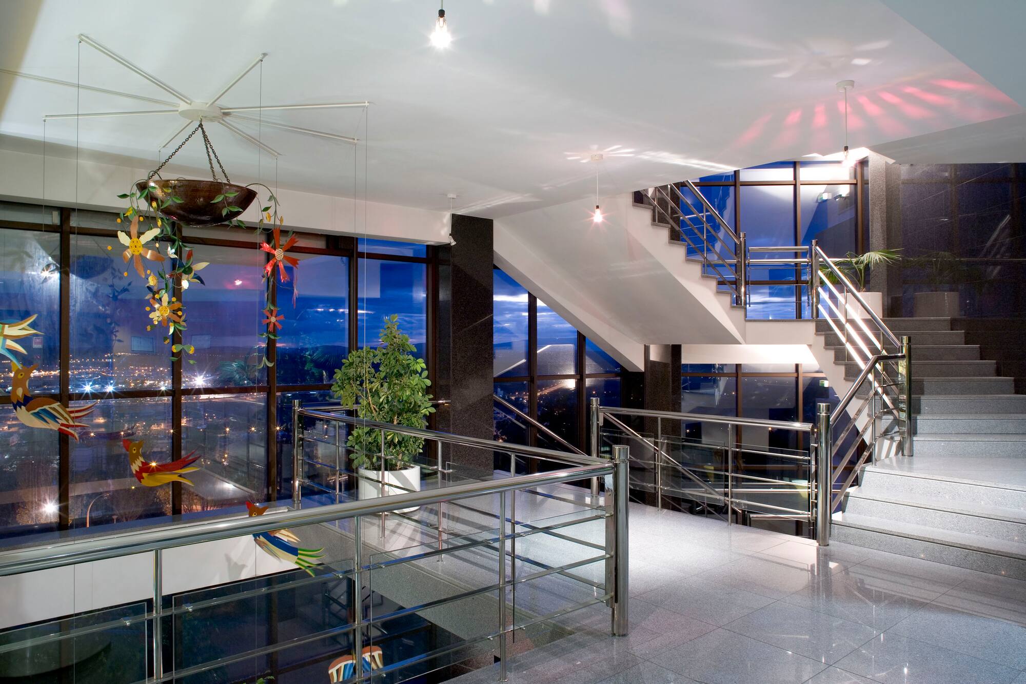 Spacious modern interior with grand staircase, city night view, chrome railings.