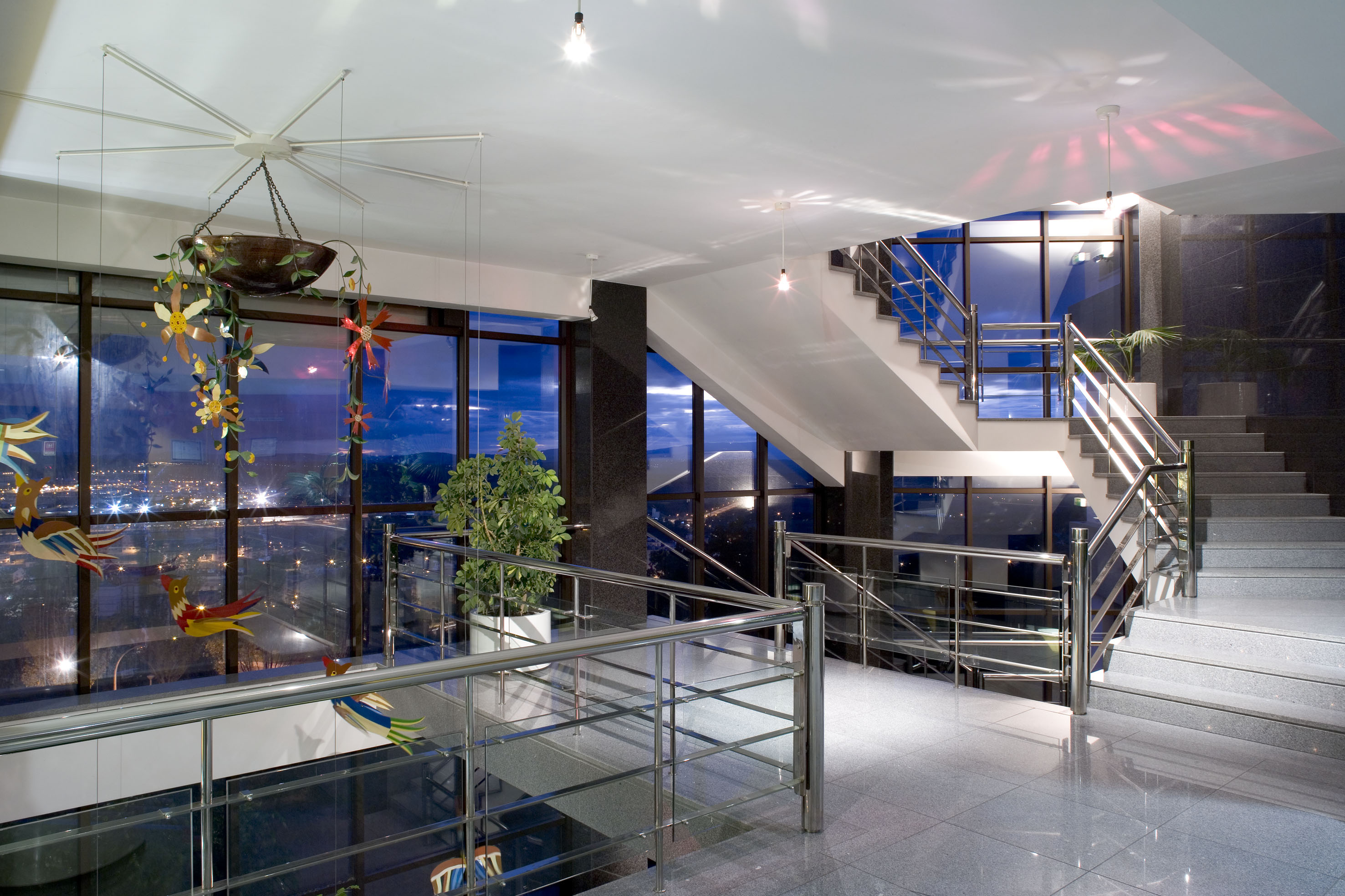 Spacious modern interior with grand staircase, city night view, chrome railings.