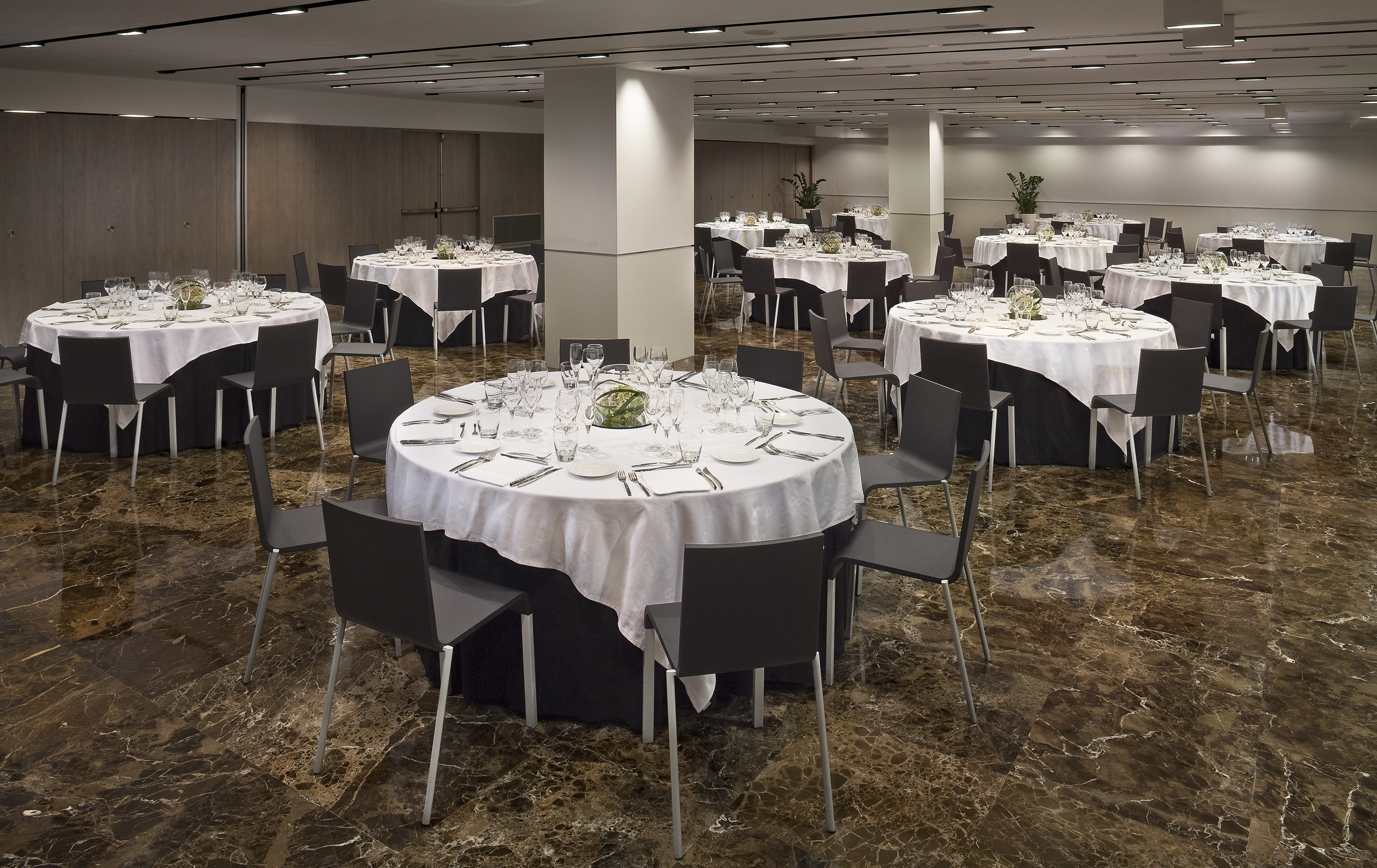 Banquet hall with round tables, white linens, dark chairs, and marble floor.