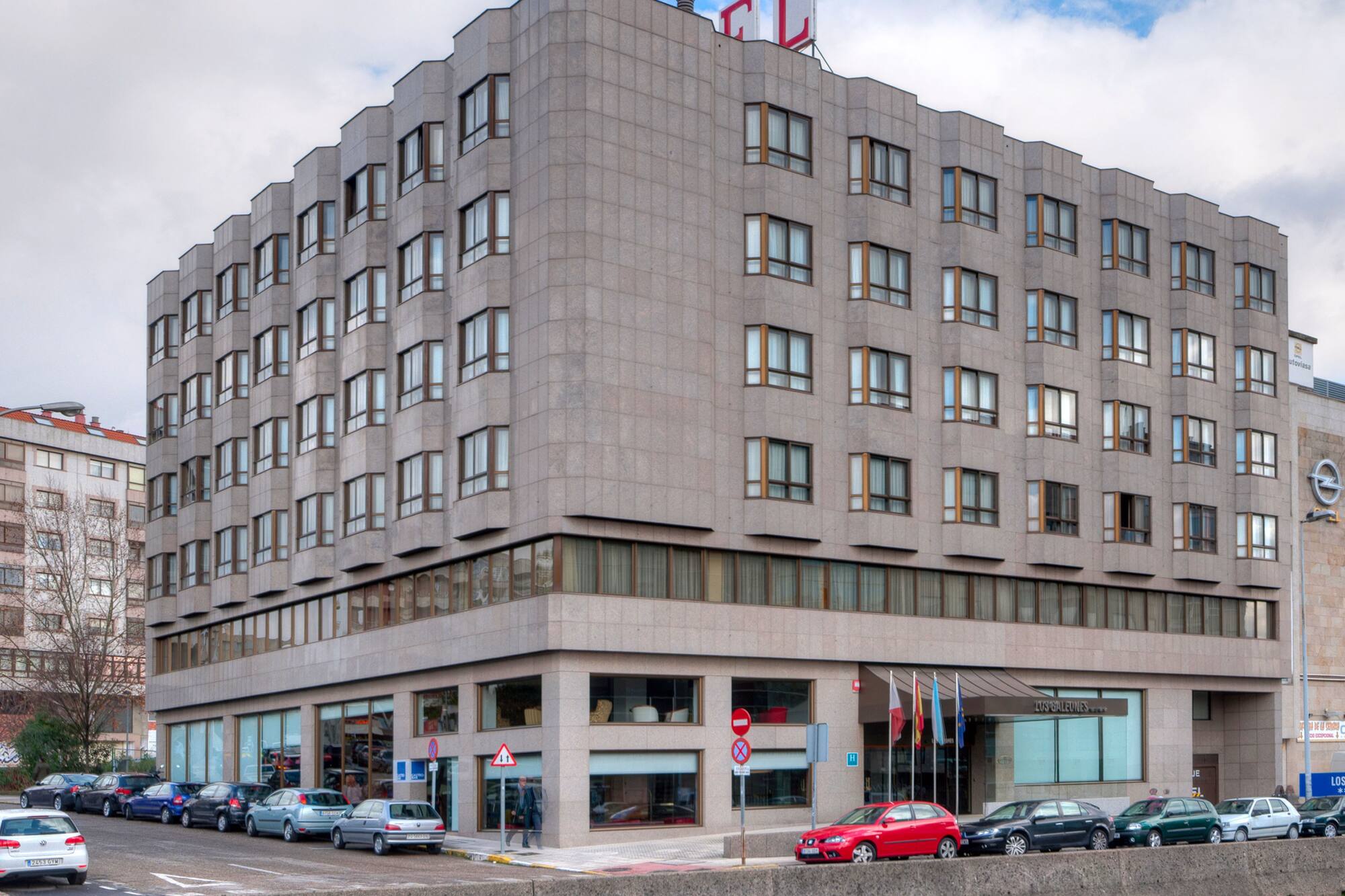 Modern hotel building with geometric grey facade, 'HOTEL' sign, and cars parked on street.