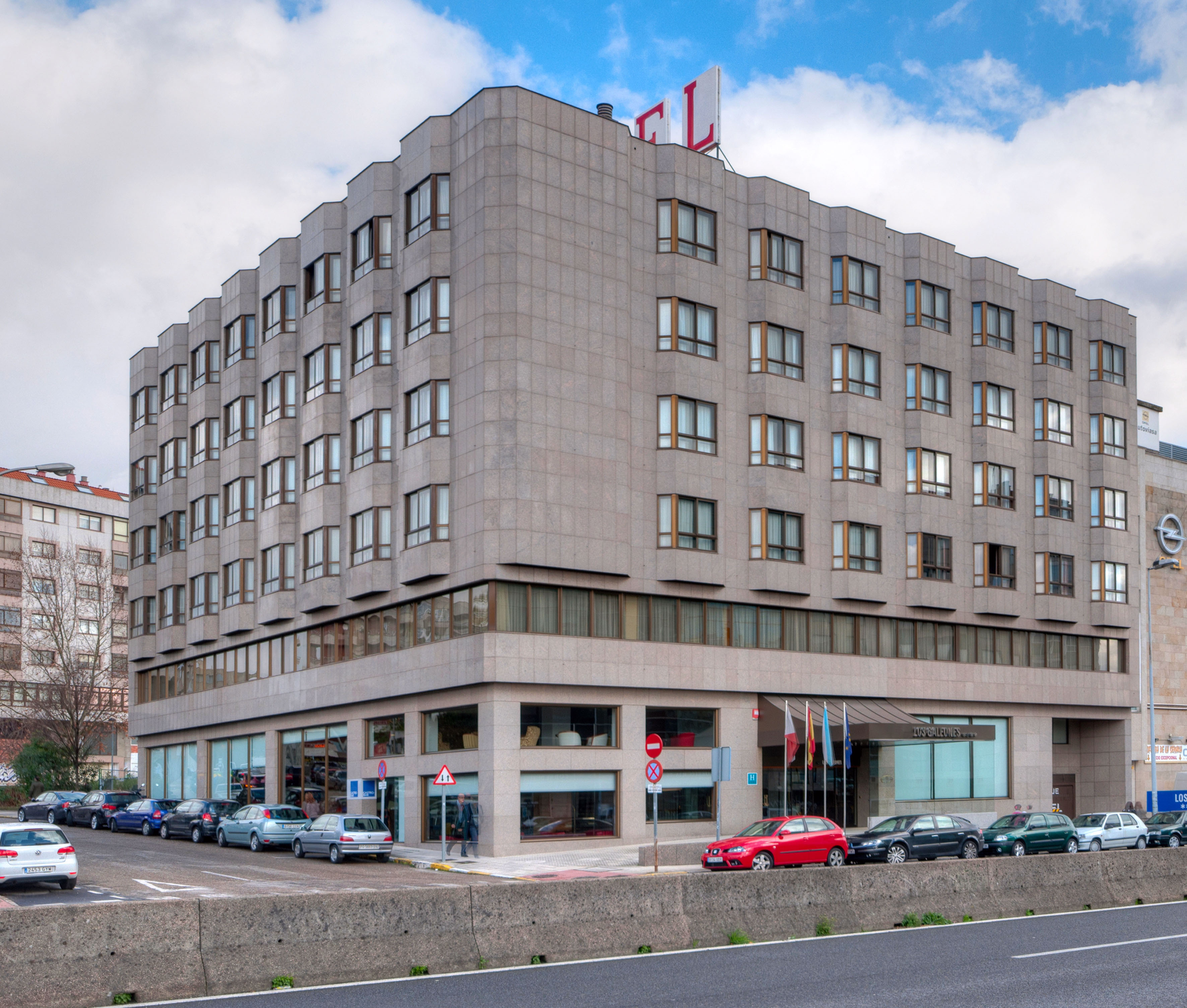 Modern hotel building with geometric grey facade, 'HOTEL' sign, and cars parked on street.