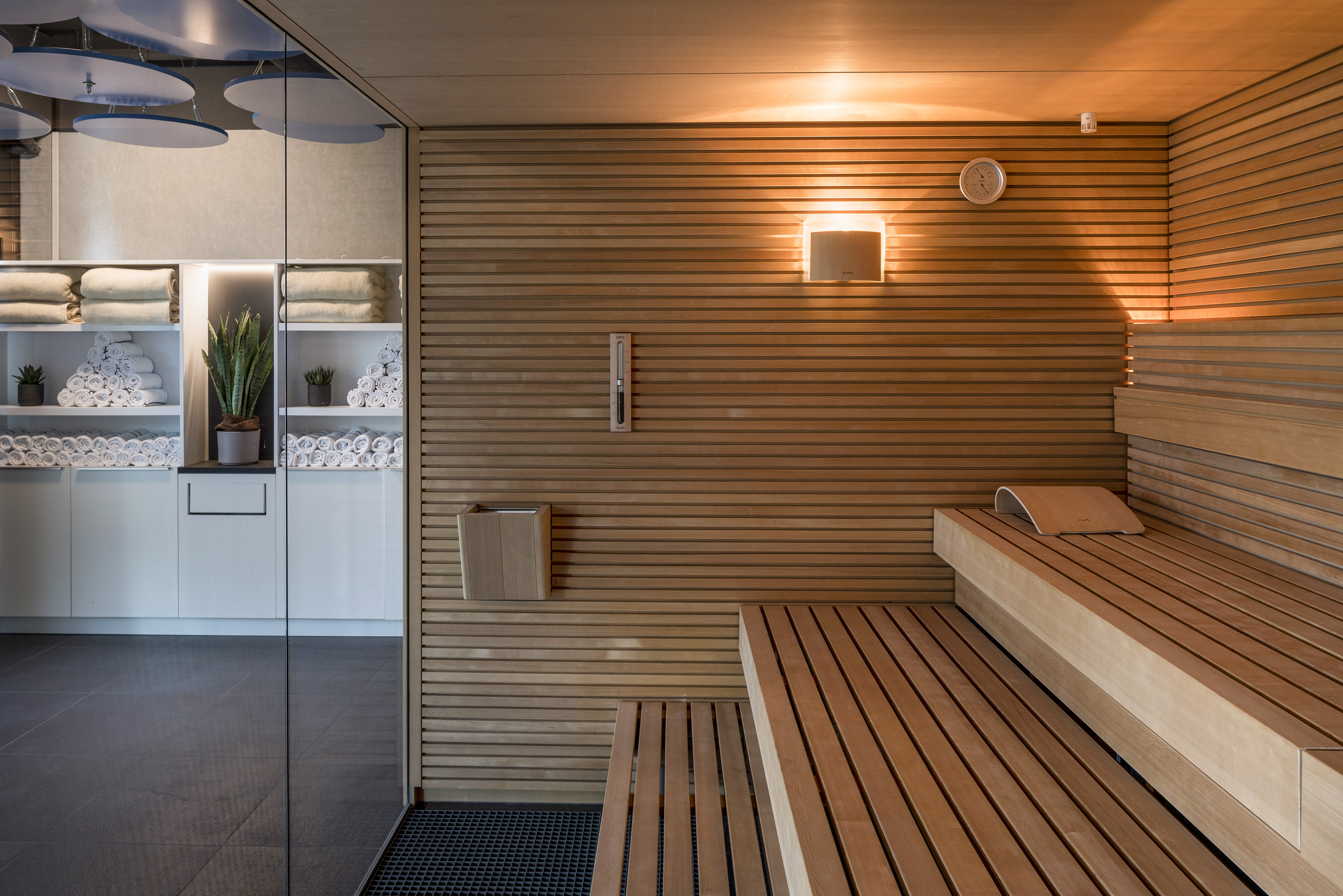 Modern wooden sauna with slatted benches and spa storage with towels.