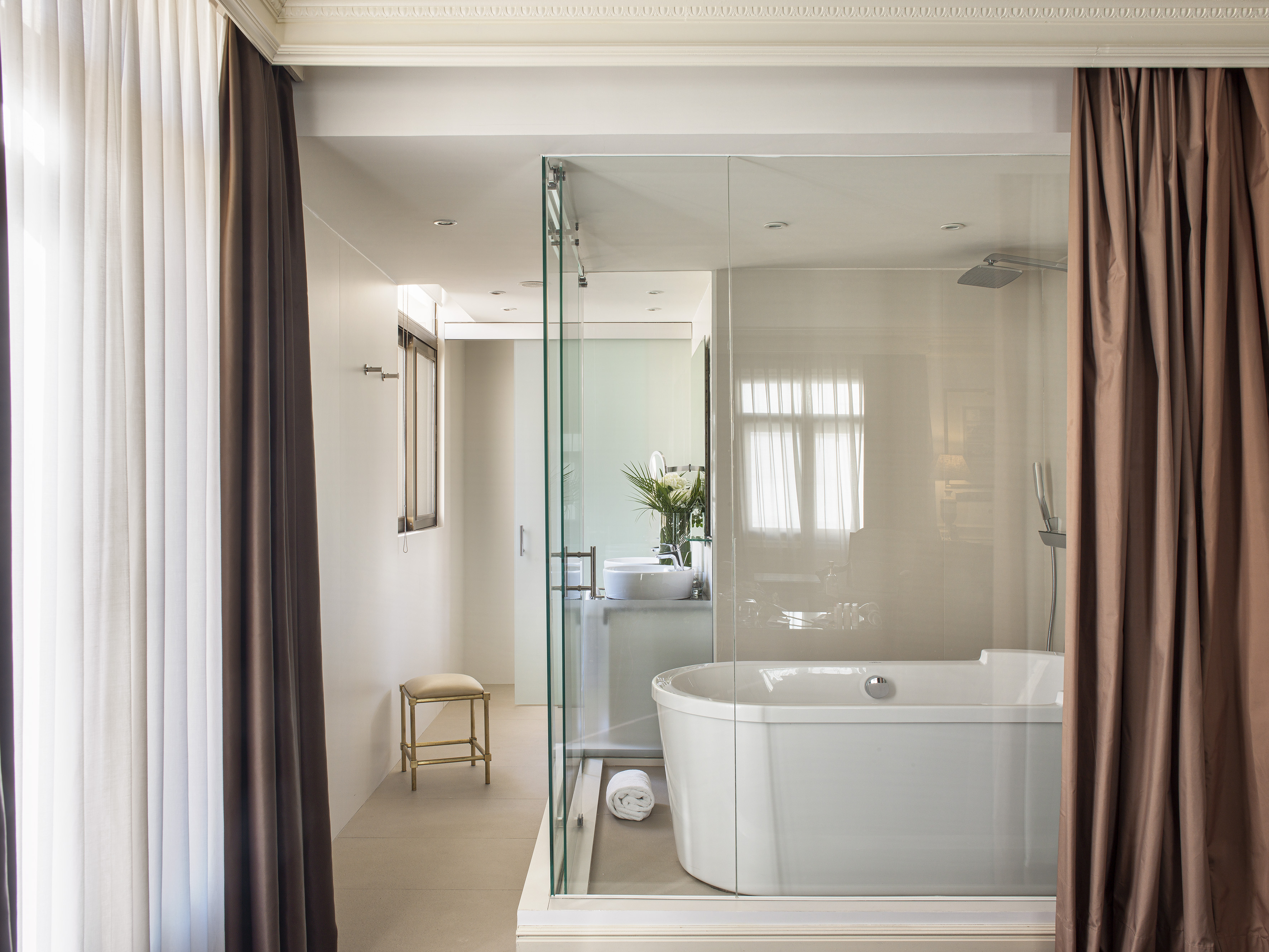 Luxury hotel bathroom with freestanding tub, glass shower, and dark brown curtains.