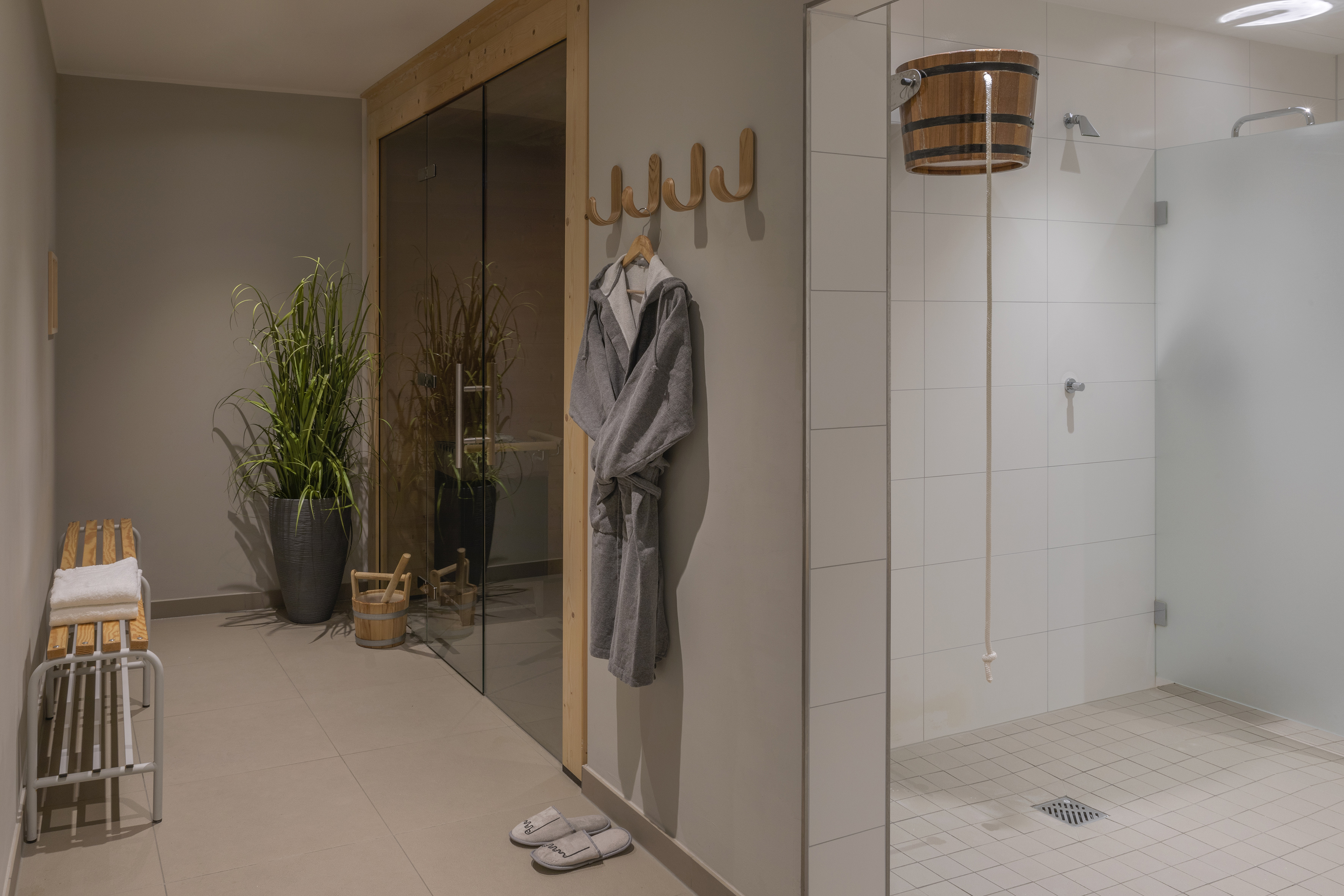 Sauna spa area with glass door, hanging bathrobe, bucket shower, and bench.
