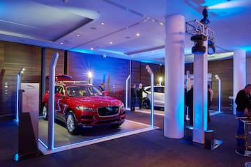 Red Jaguar F-Pace and white SUV on display with blue event lighting.