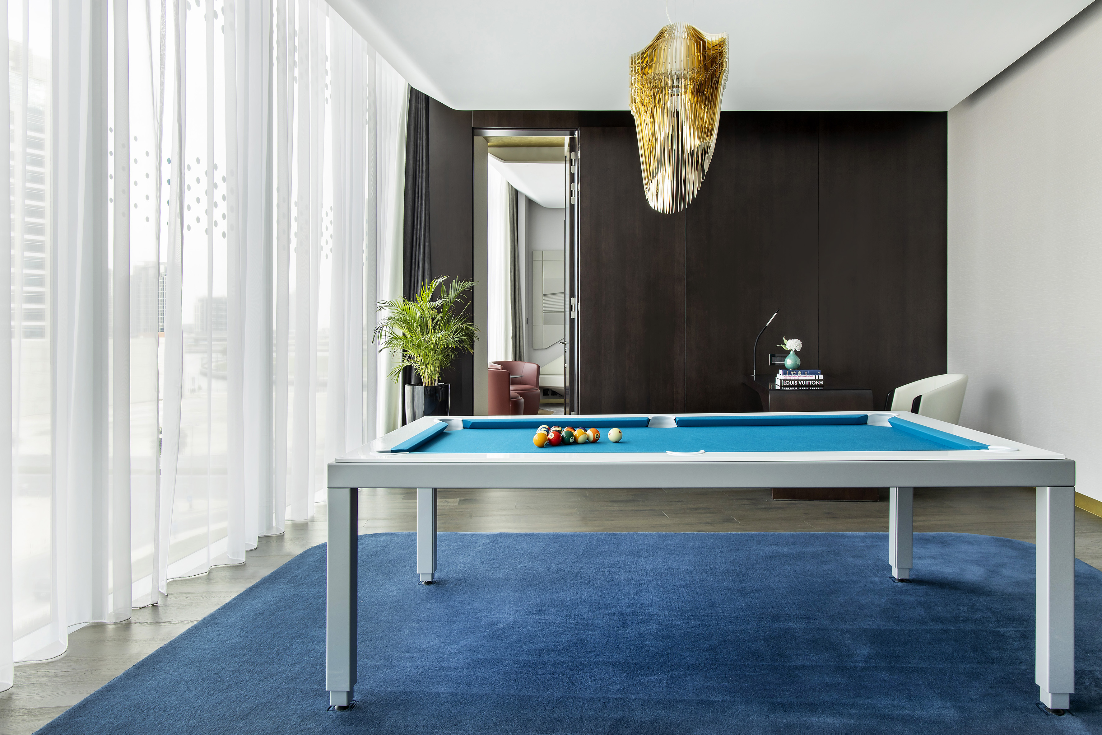 Luxury modern pool table with blue felt, white frame, blue rug, and gold chandelier.
