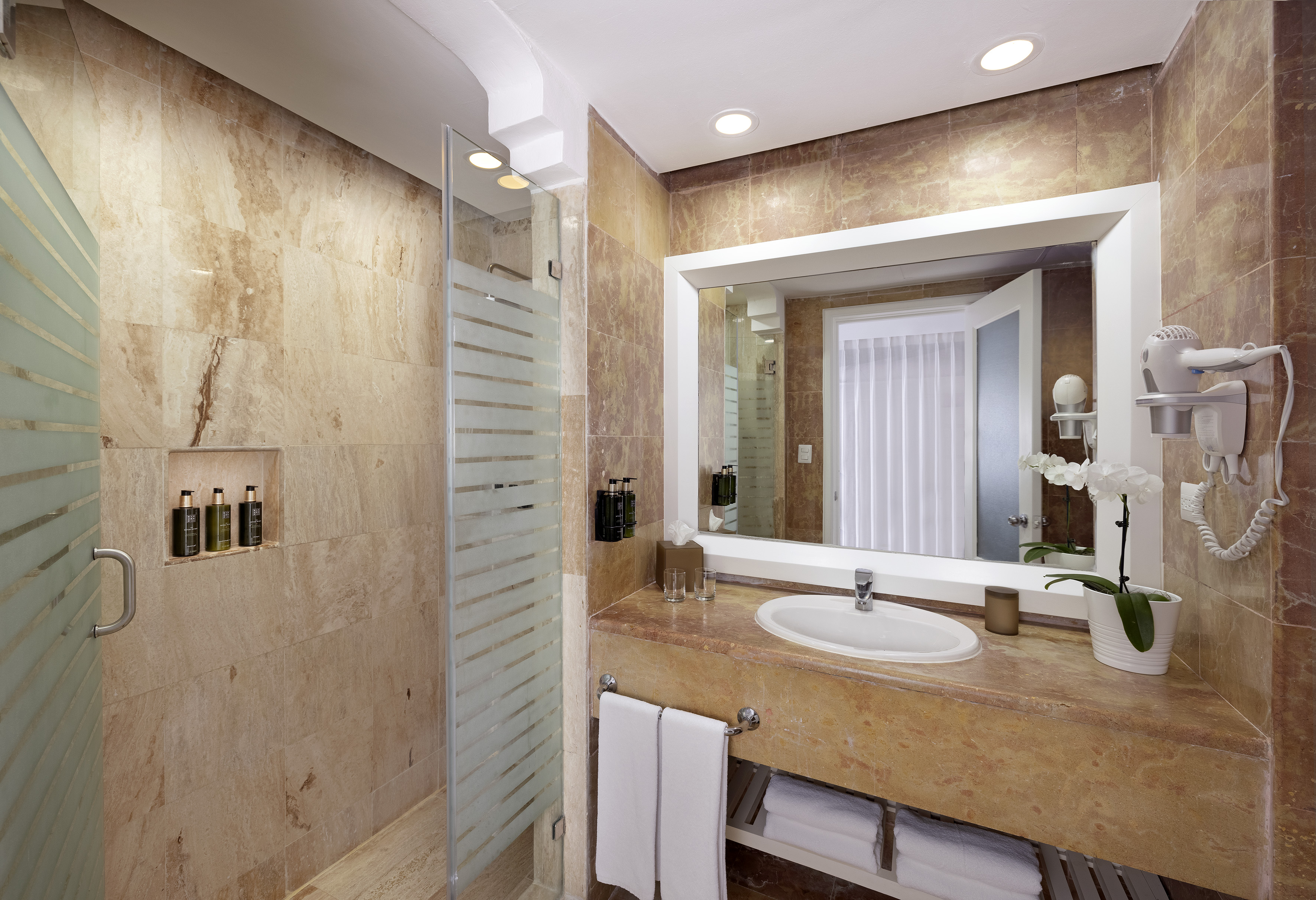 Modern marble bathroom with glass shower, vanity, sink, and white towels.