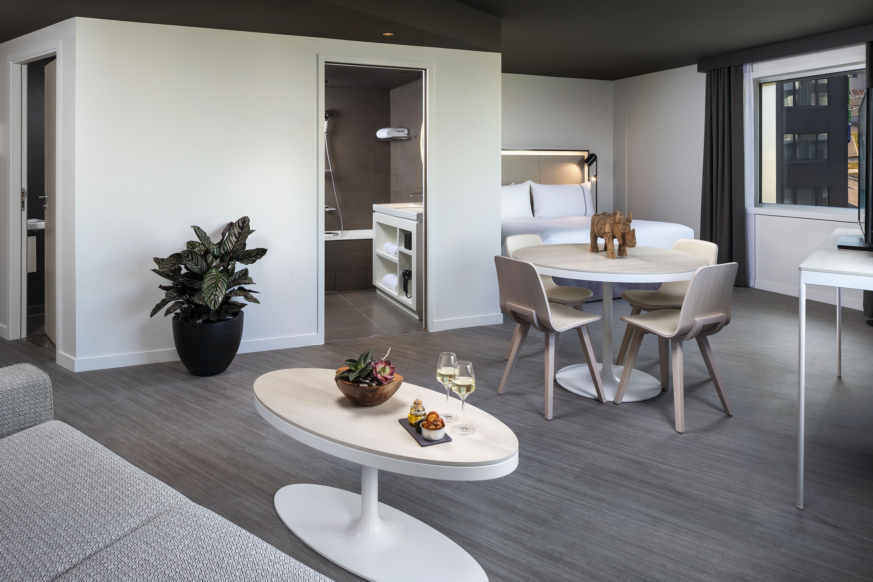 Modern hotel suite: living room, dining area, bedroom, and open bathroom.
