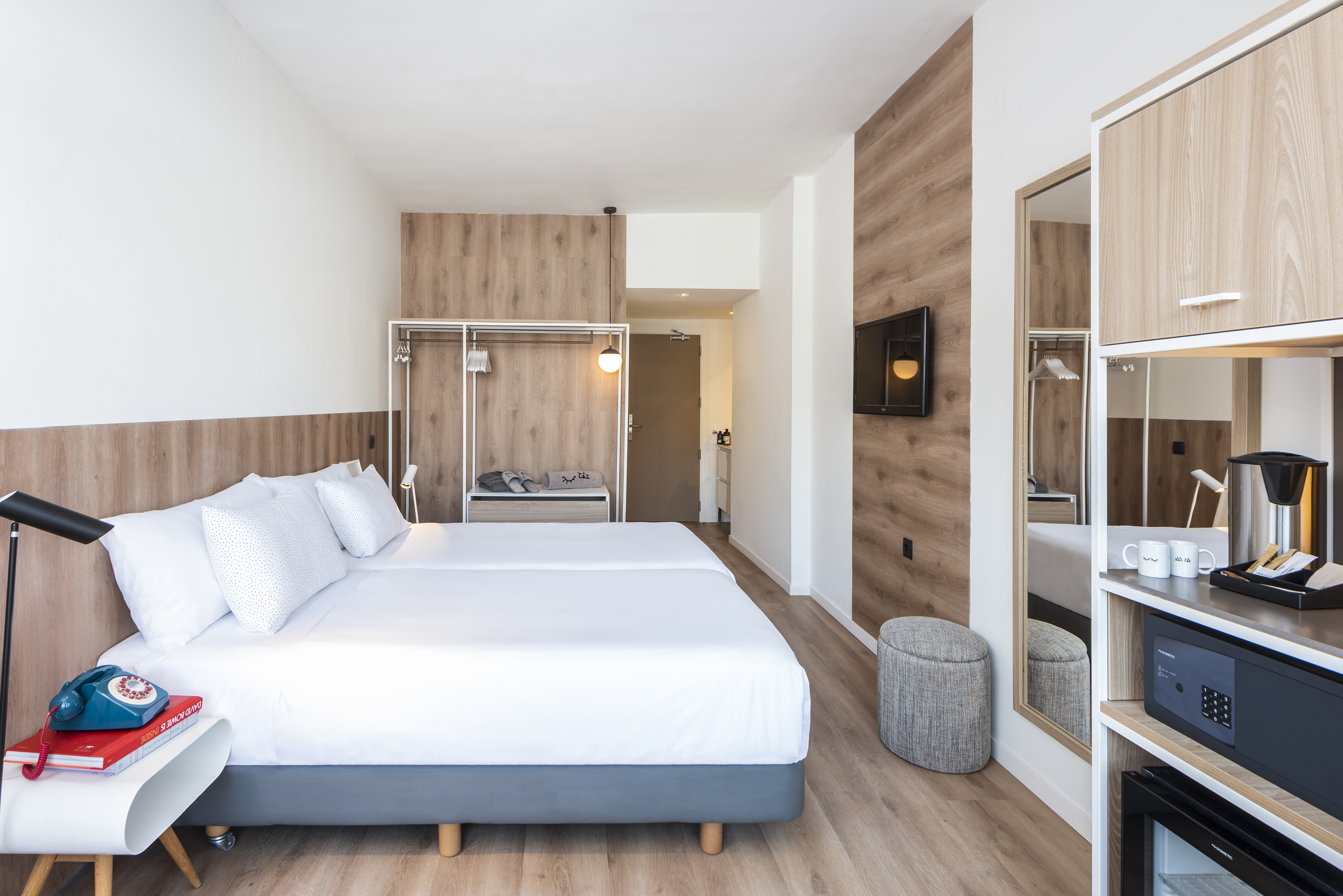 Modern hotel room with twin beds, wood accents, and a coffee station.