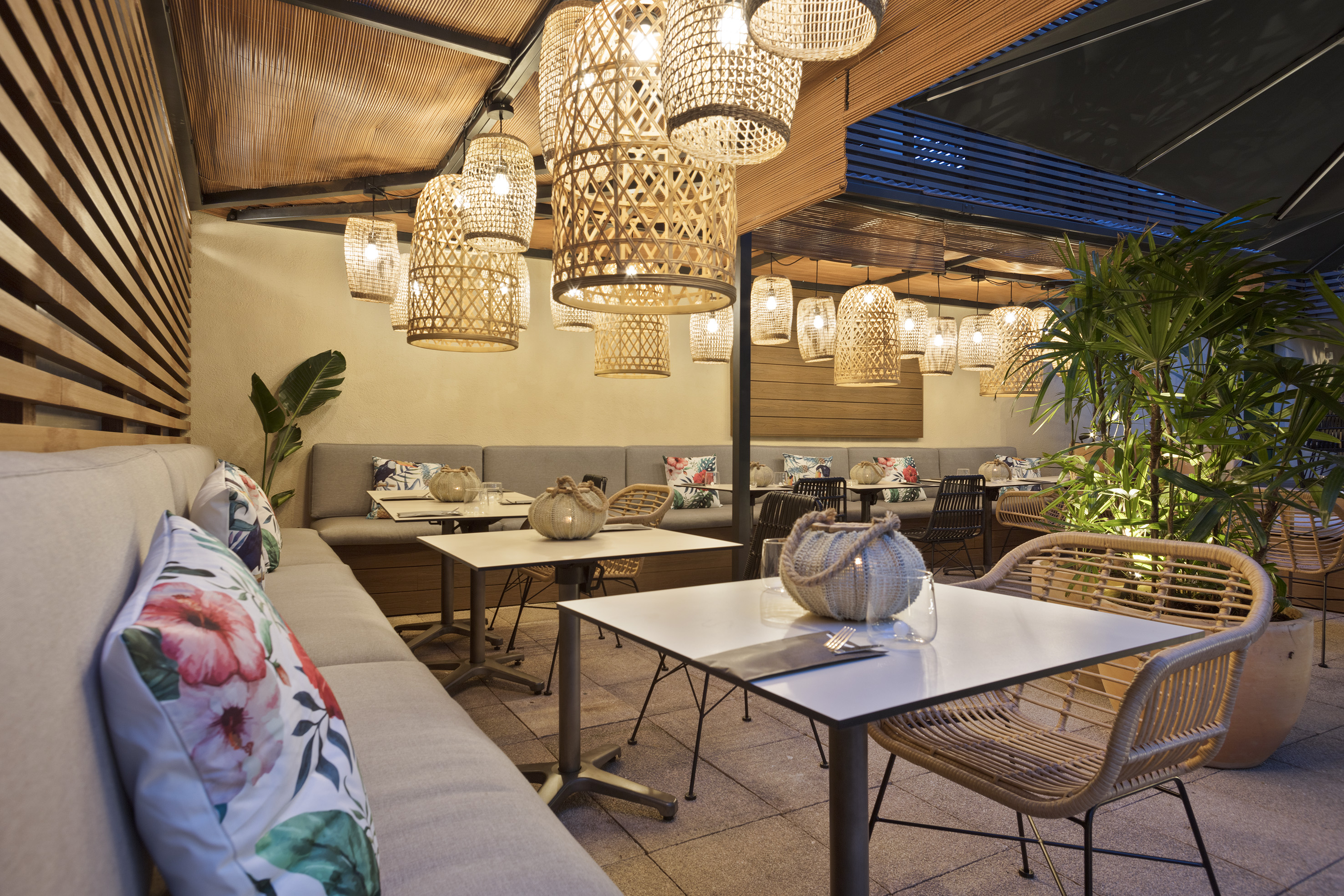 Stylish outdoor restaurant patio with rattan pendant lights and tropical decor.
