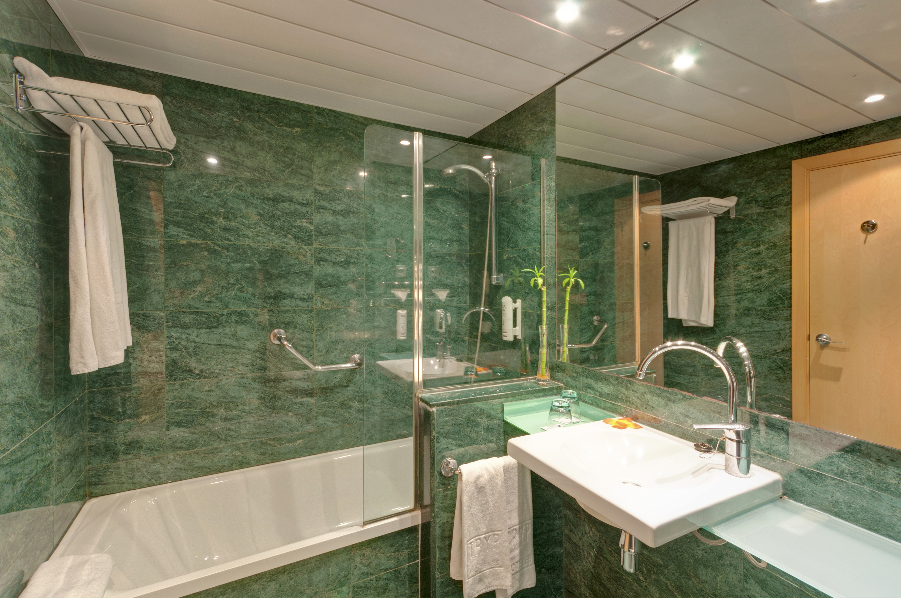 Modern hotel bathroom featuring green marble tiles, bathtub, shower, and sink.