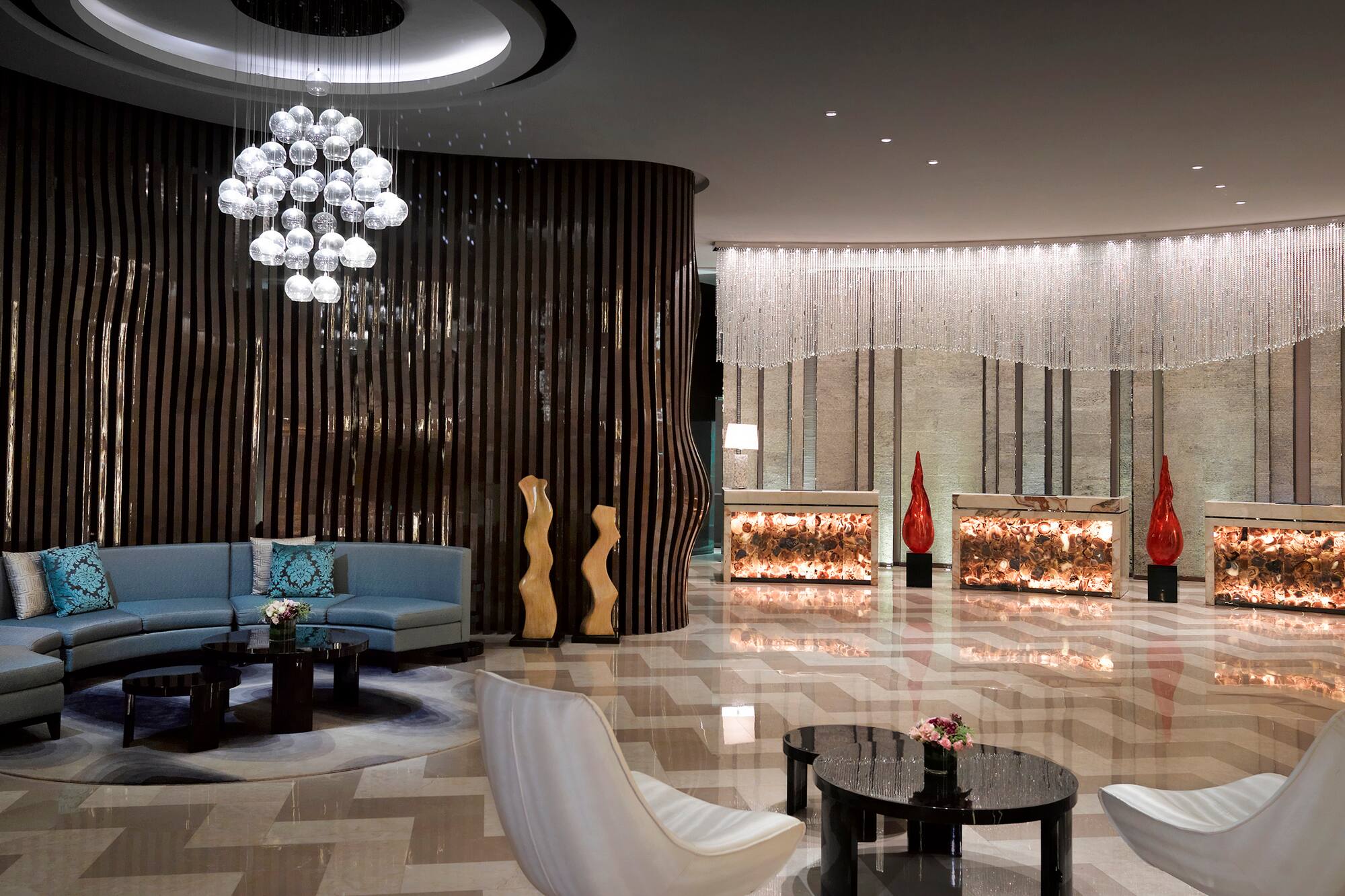 Modern luxury hotel lobby with bubble chandelier and illuminated reception.