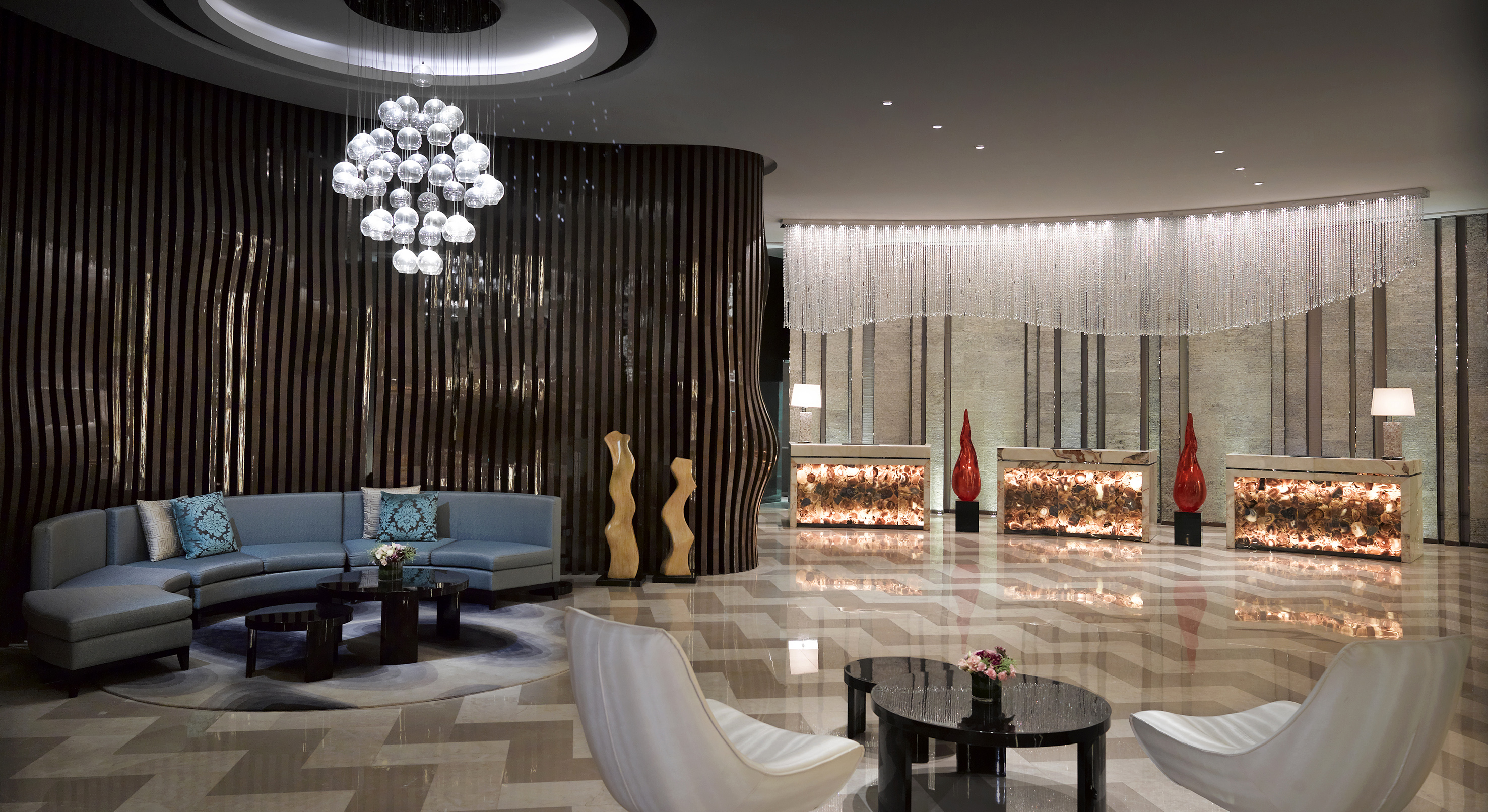 Modern luxury hotel lobby with bubble chandelier and illuminated reception.