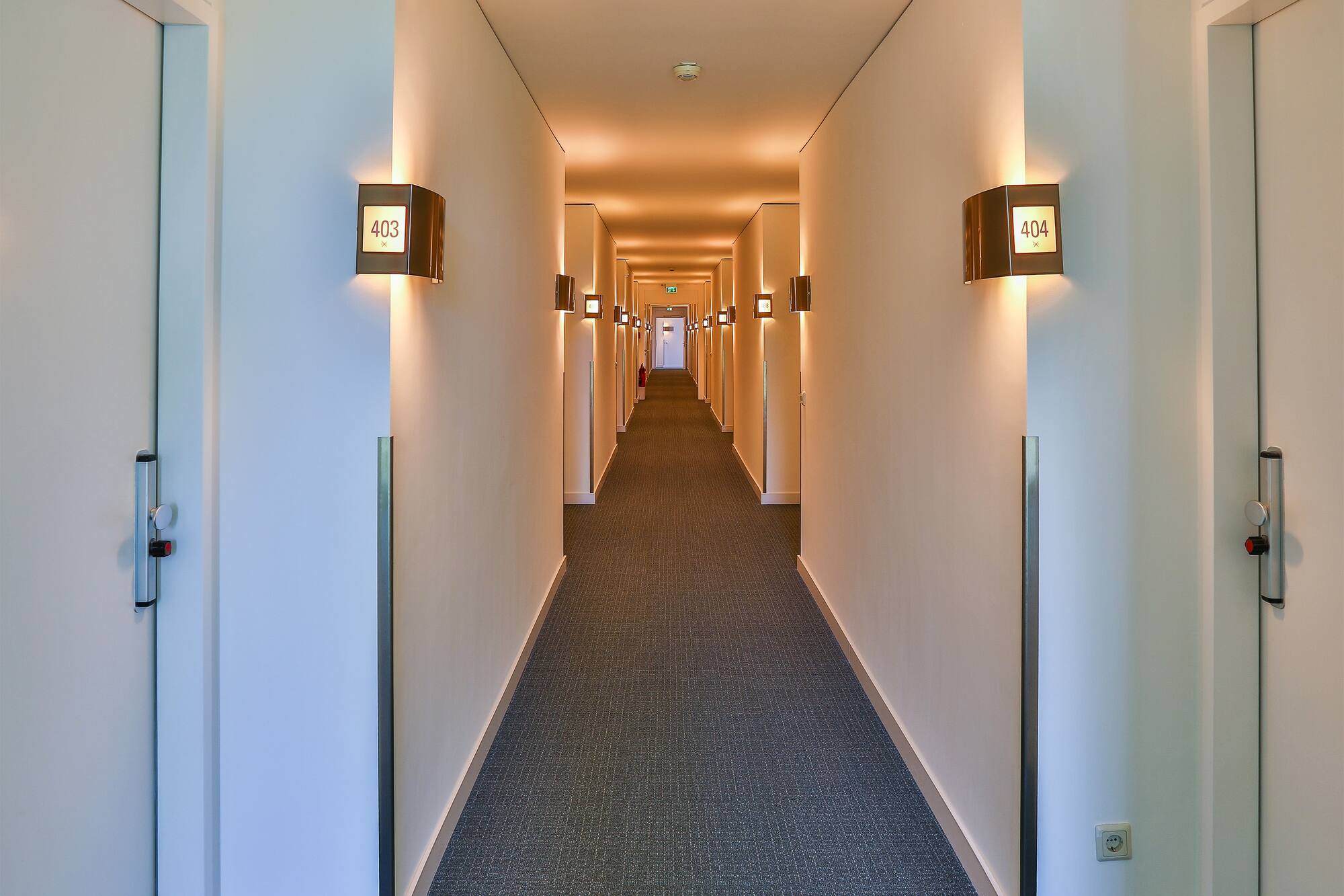 Modern hotel hallway with illuminated room numbers and warm lighting.