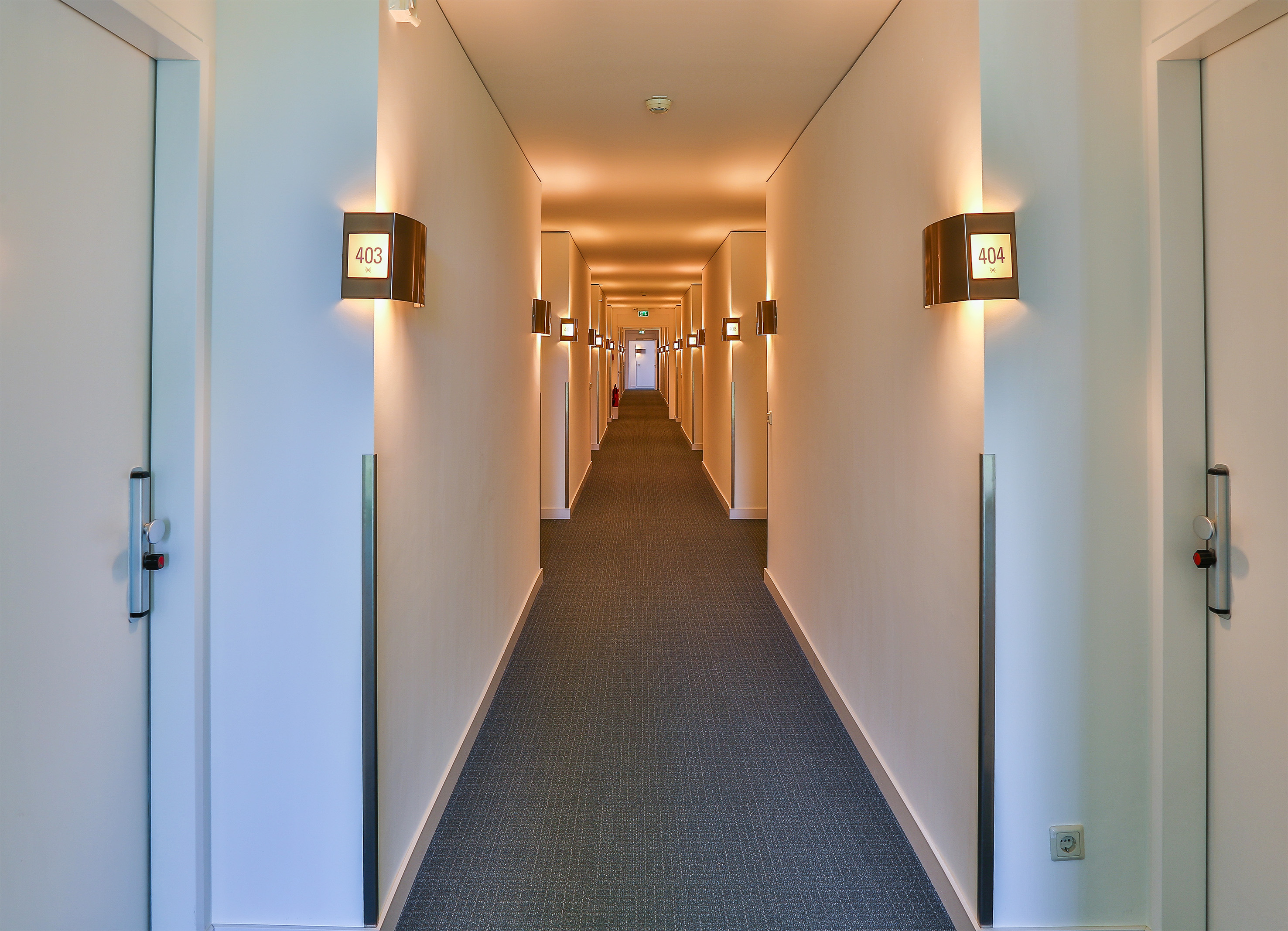 Modern hotel hallway with illuminated room numbers and warm lighting.