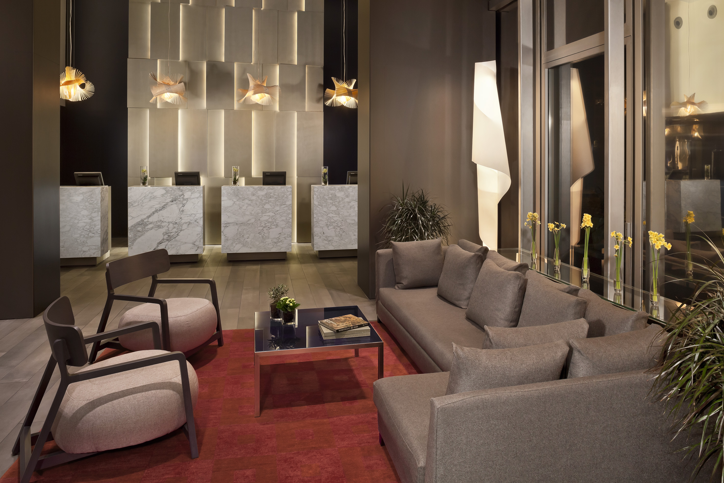 Modern hotel lobby with marble reception desks, gray sofa, and stylish lighting.