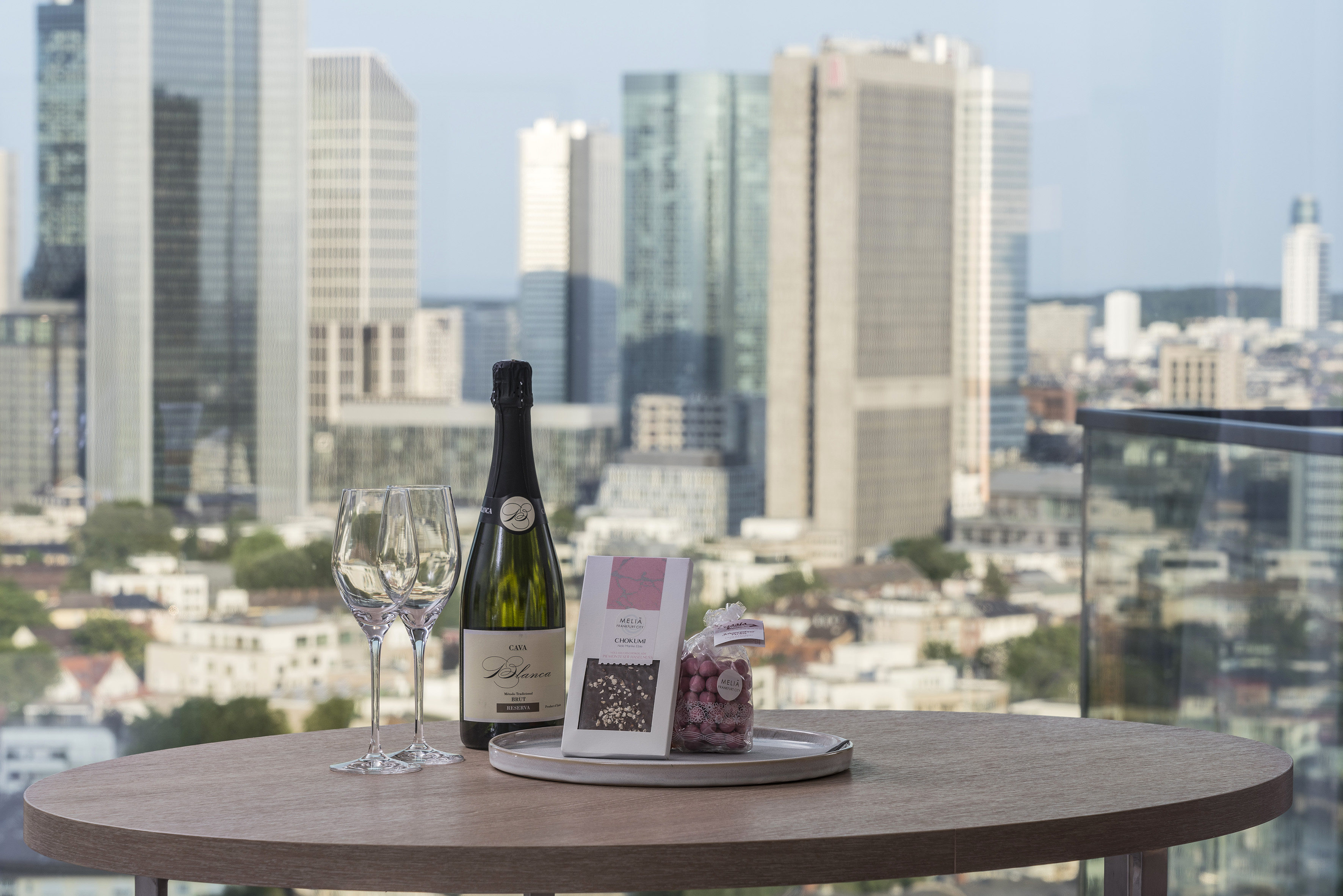 Sparkling wine, glasses, and chocolates on a table with city skyline view.