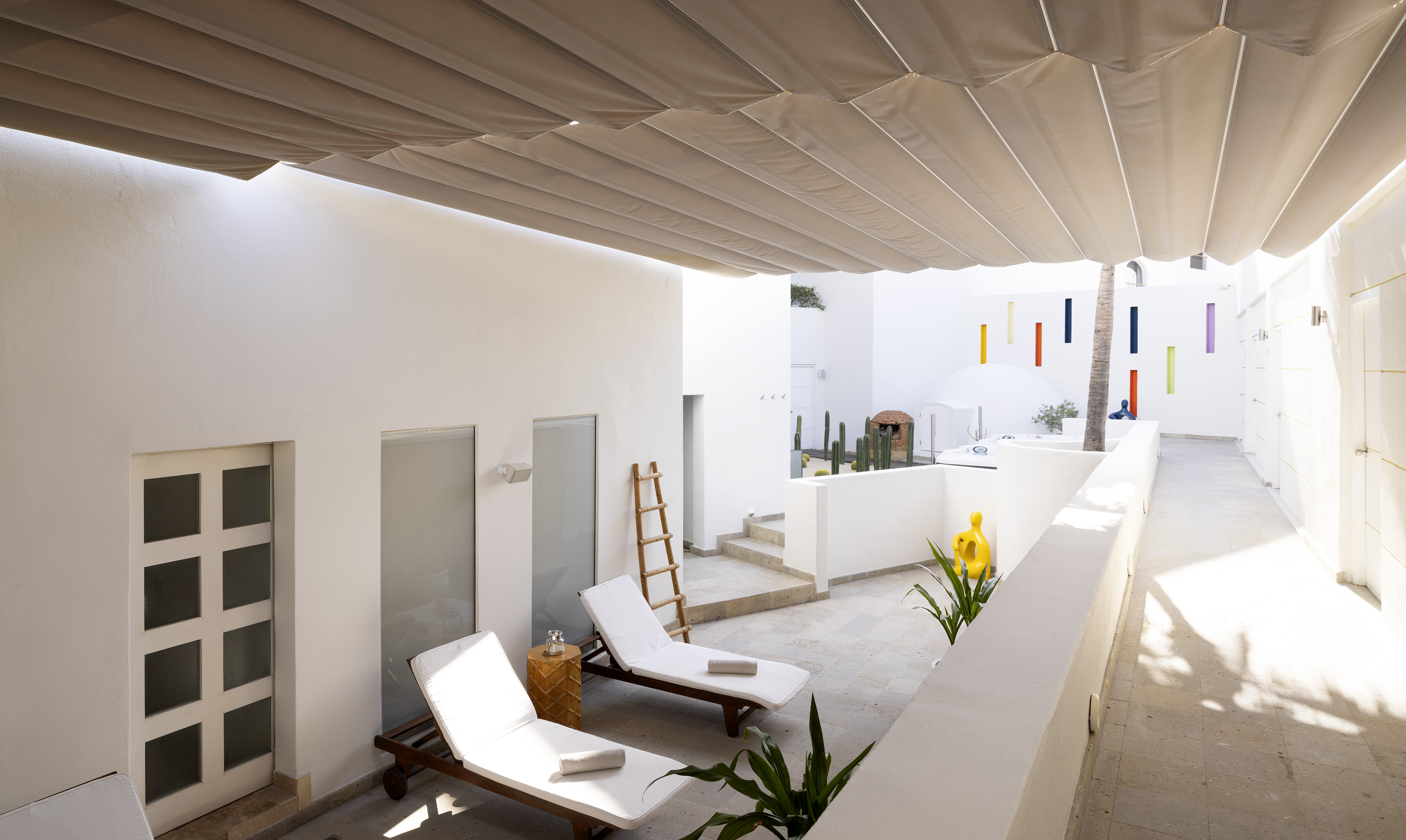 Minimalist white patio with retractable awning, two sun loungers, and succulents.