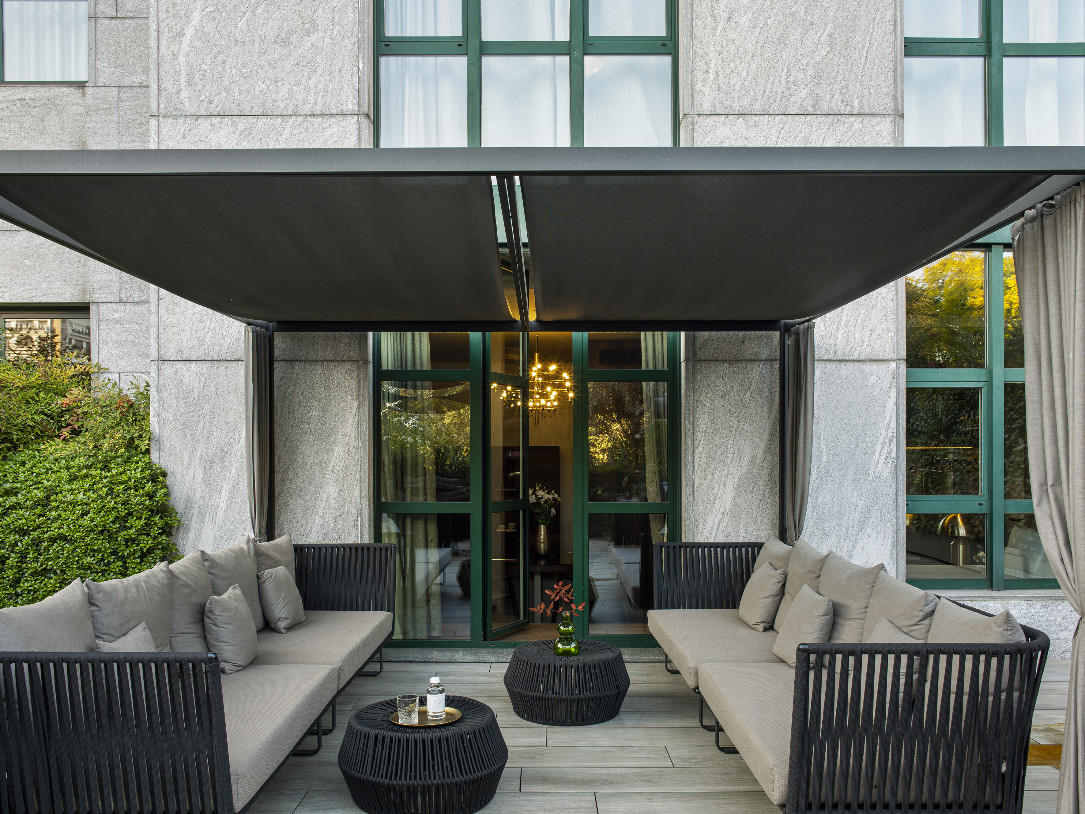 Modern outdoor patio with grey sofas, woven tables, and retractable canopy.