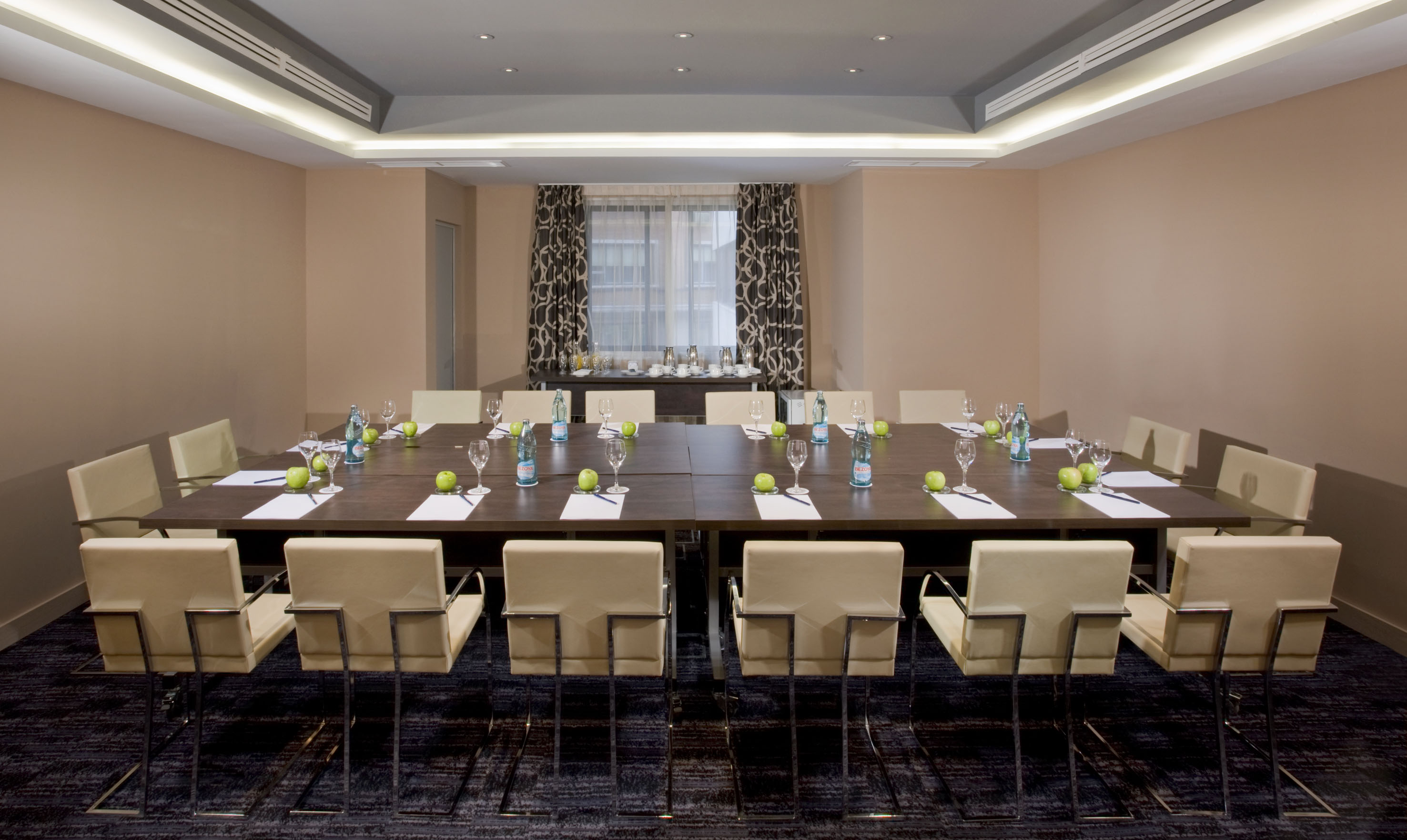 Modern conference room with large table, cream chairs, water, and apples.