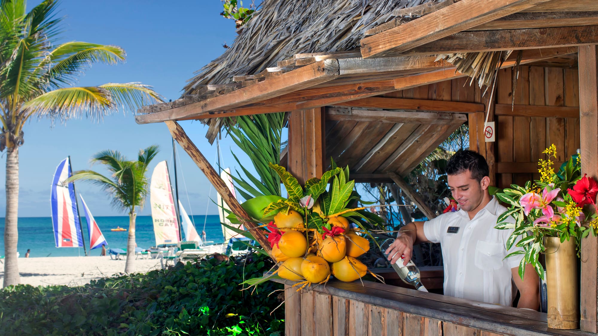 a man pouring a drink from a bottle at a beach bar
