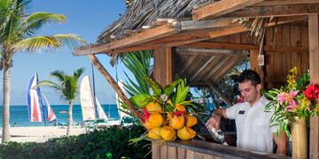 a man pouring a drink from a bottle at a beach bar