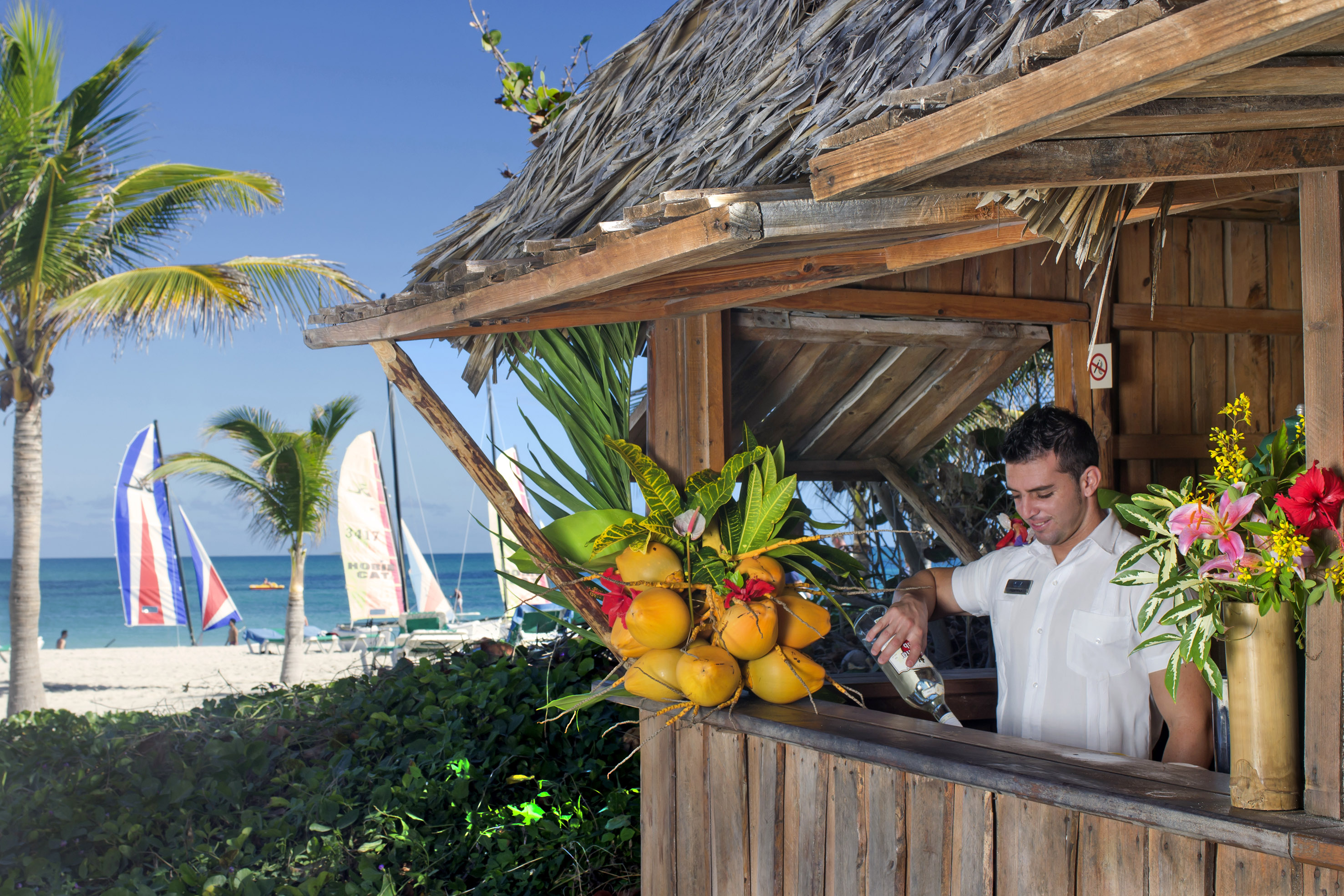 a man pouring a drink from a bottle at a beach bar