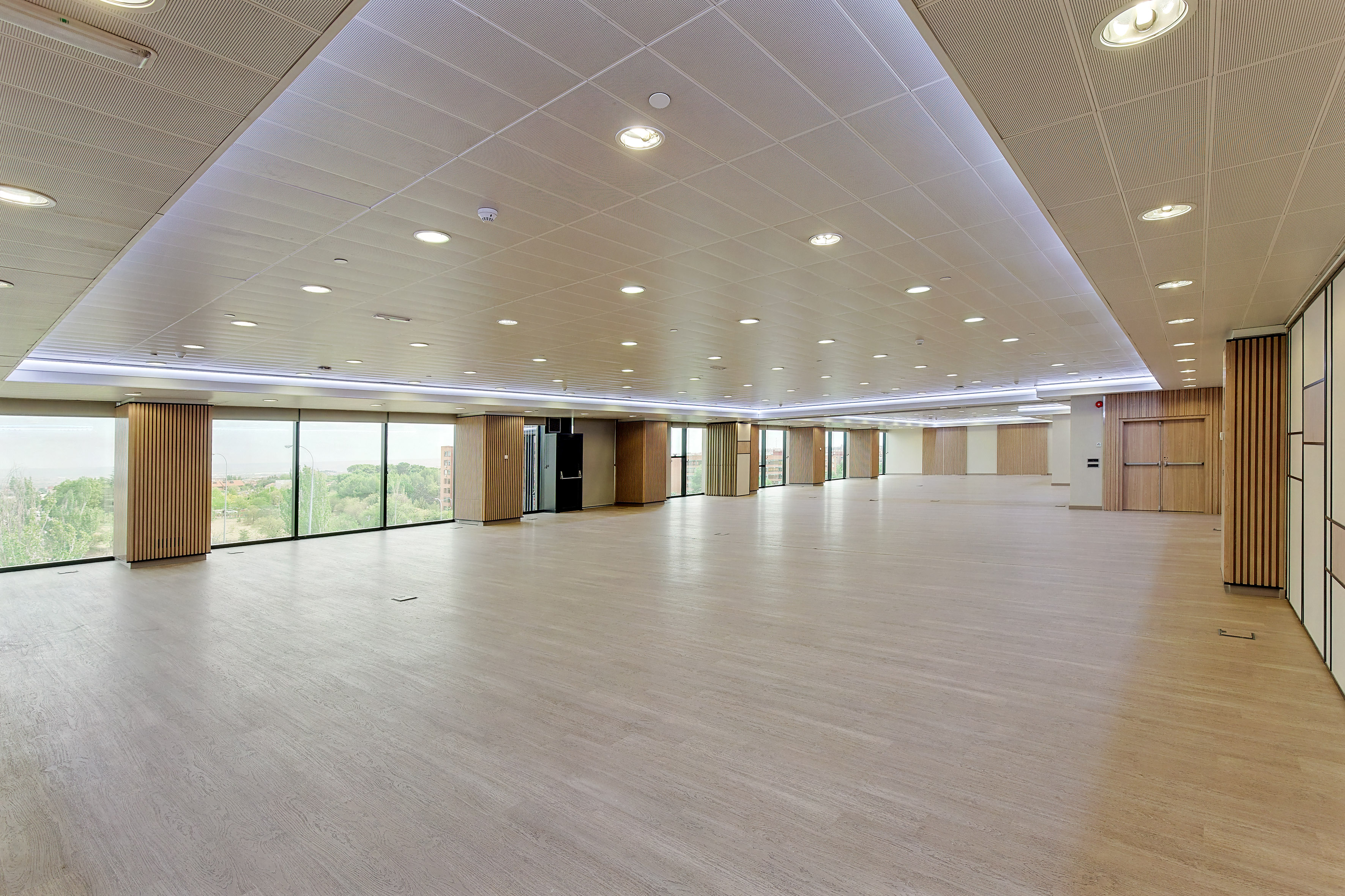 Spacious modern conference hall with wooden floor, large windows, and bright lighting.