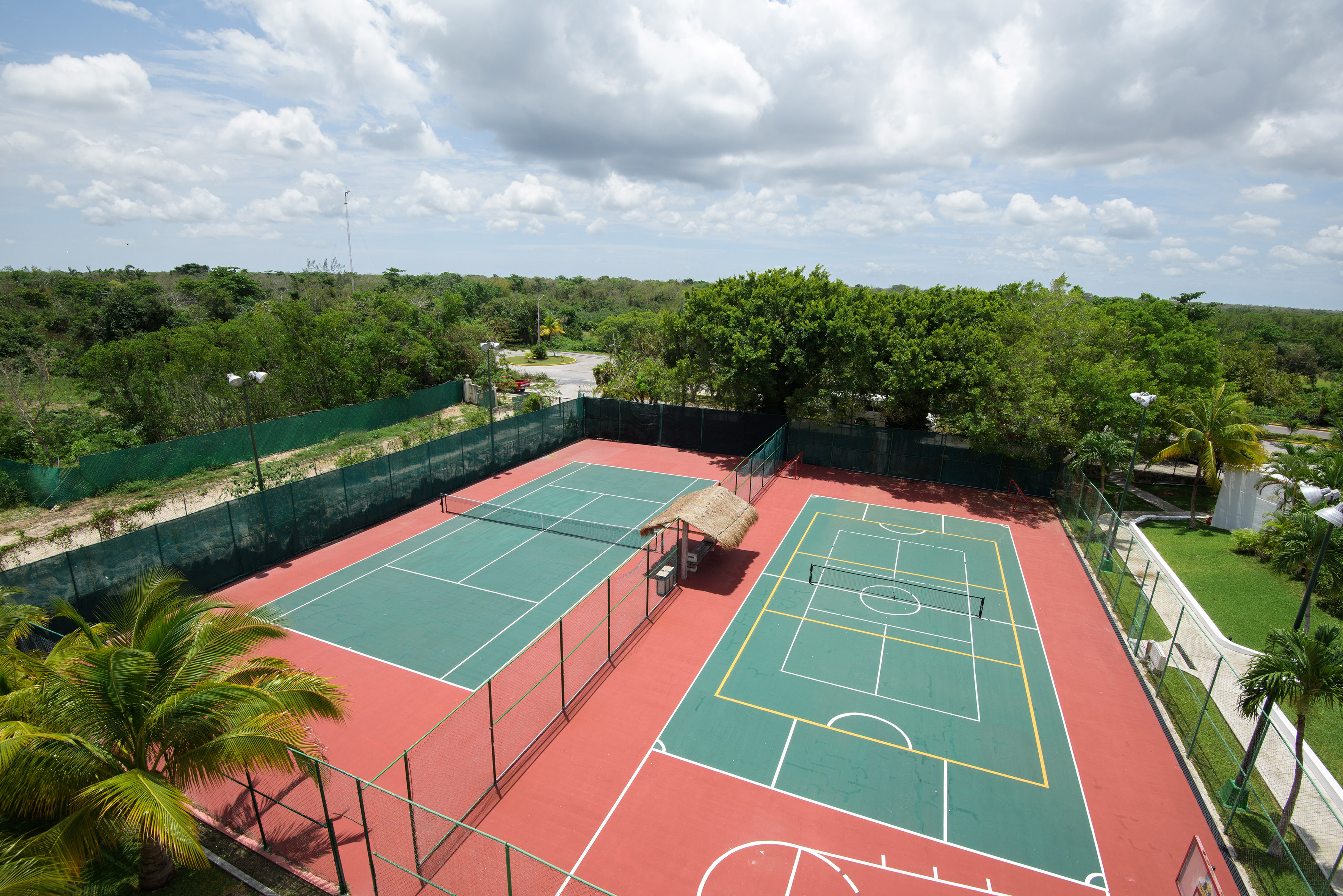 Canchas de tenis y multideportiva rojas y verdes en resort tropical, vista aérea.