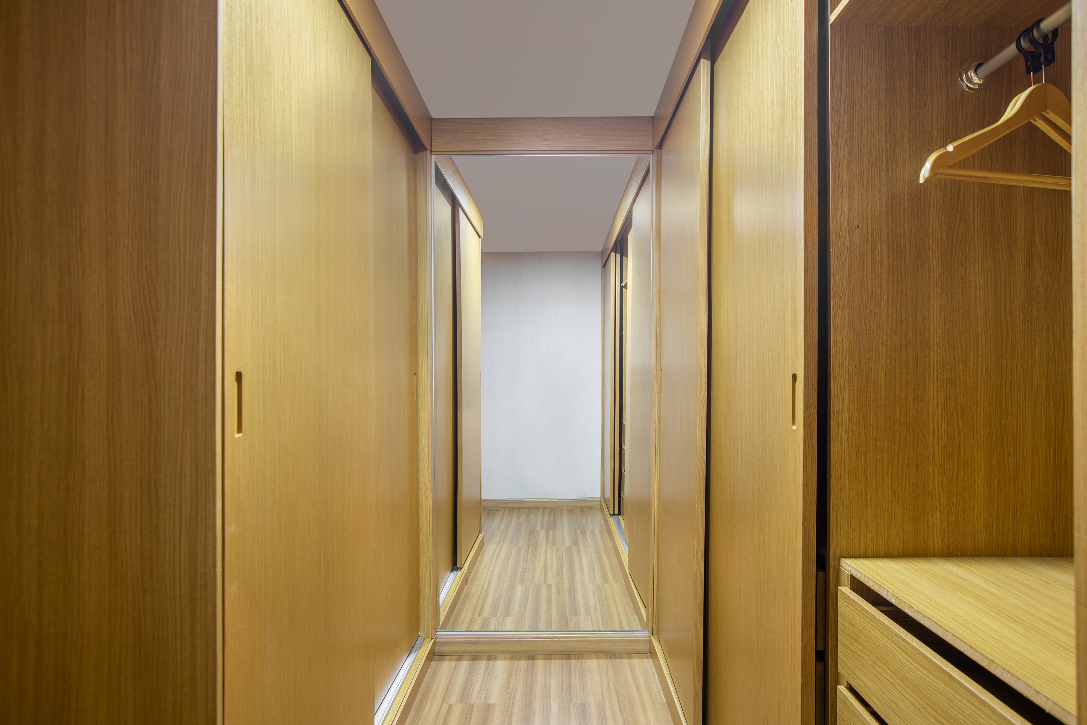 Light wood walk-in closet with sliding doors, built-in storage, and mirror.