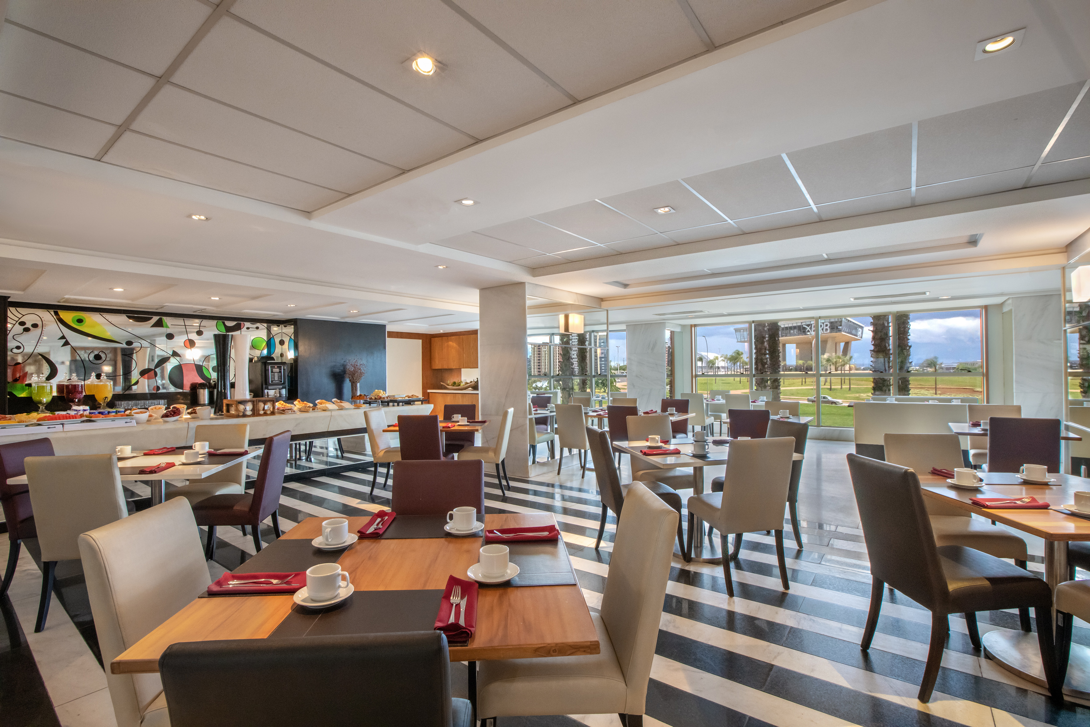 Modern restaurant with black-white floor, buffet, set tables, garden view.