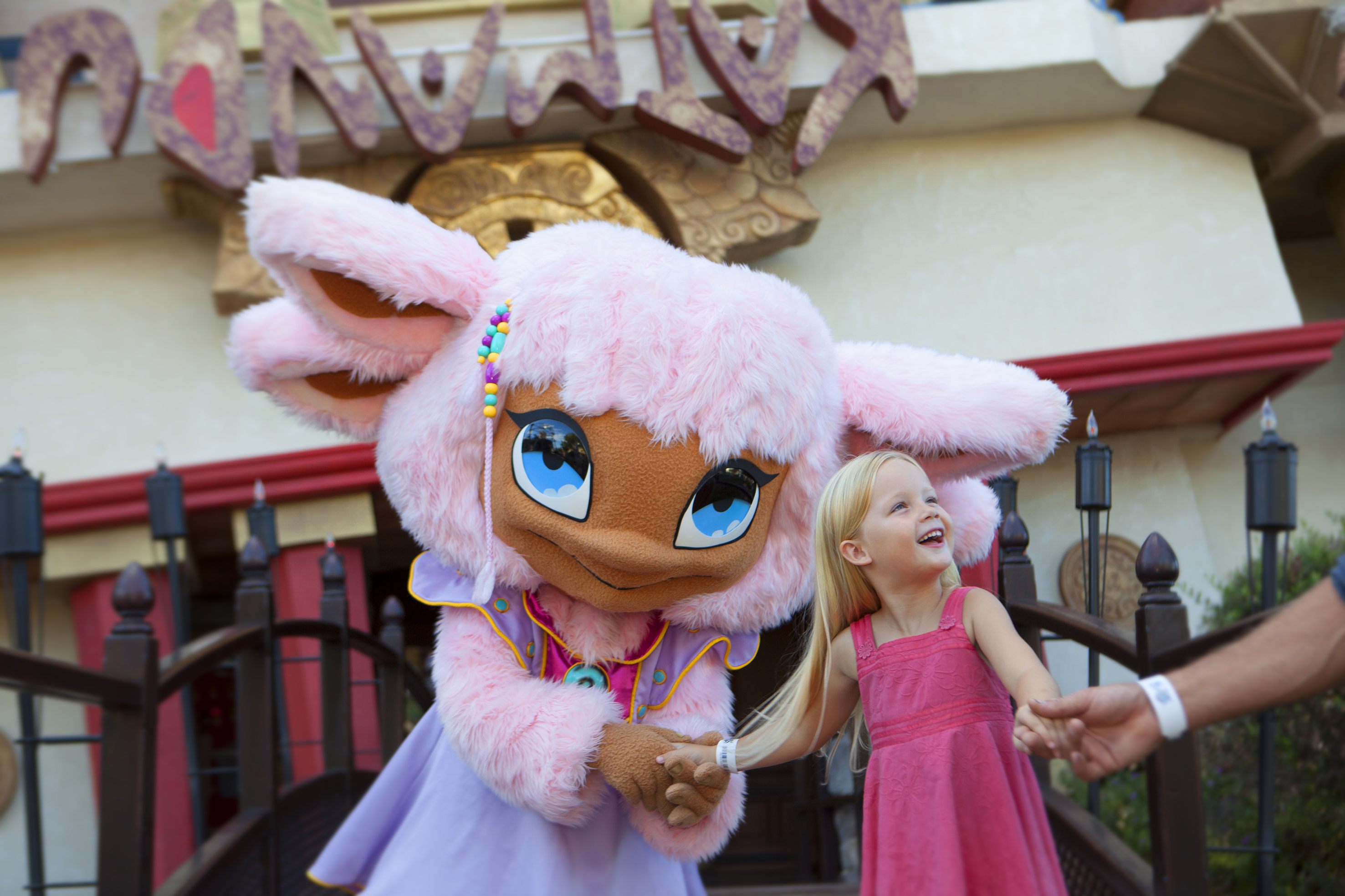 Happy blonde girl and pink mascot character at theme park.