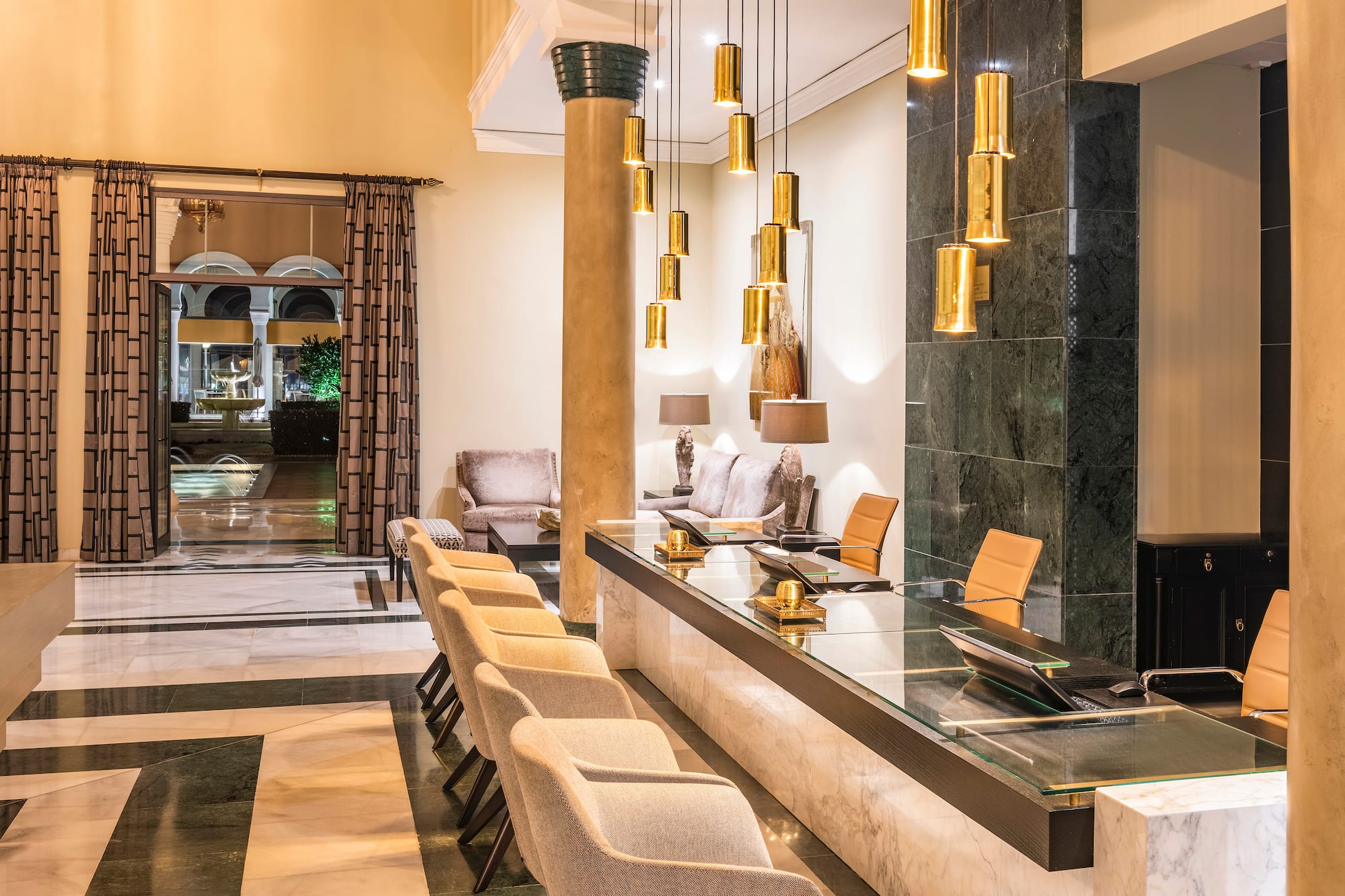 Luxury hotel lobby with marble reception desk, gold pendant lights, and patterned floor.